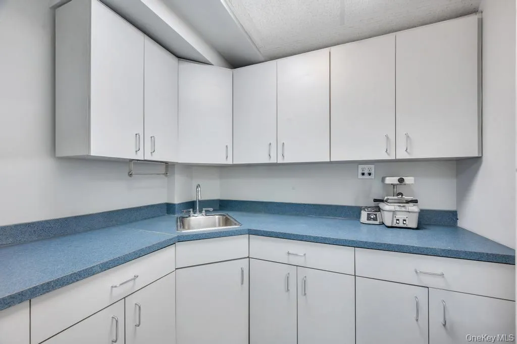 Corner workstation featuring extensive white cabinetry, speckled blue countertops, and an integrated stainless steel sink with a chrome faucet Corner workstation featuring extensive white cabinetry, speckled blue countertops, and an integrated stainless steel sink with a chrome faucet