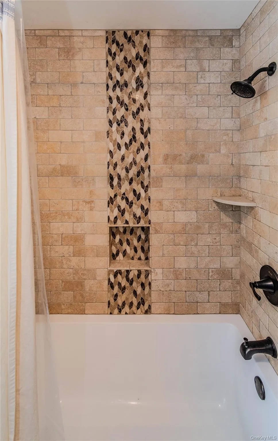 Tiled shower surround with decorative mosaic inlay, two recessed niches, and dark bronze fixtures Tiled shower surround with decorative mosaic inlay, two recessed niches, and dark bronze fixtures