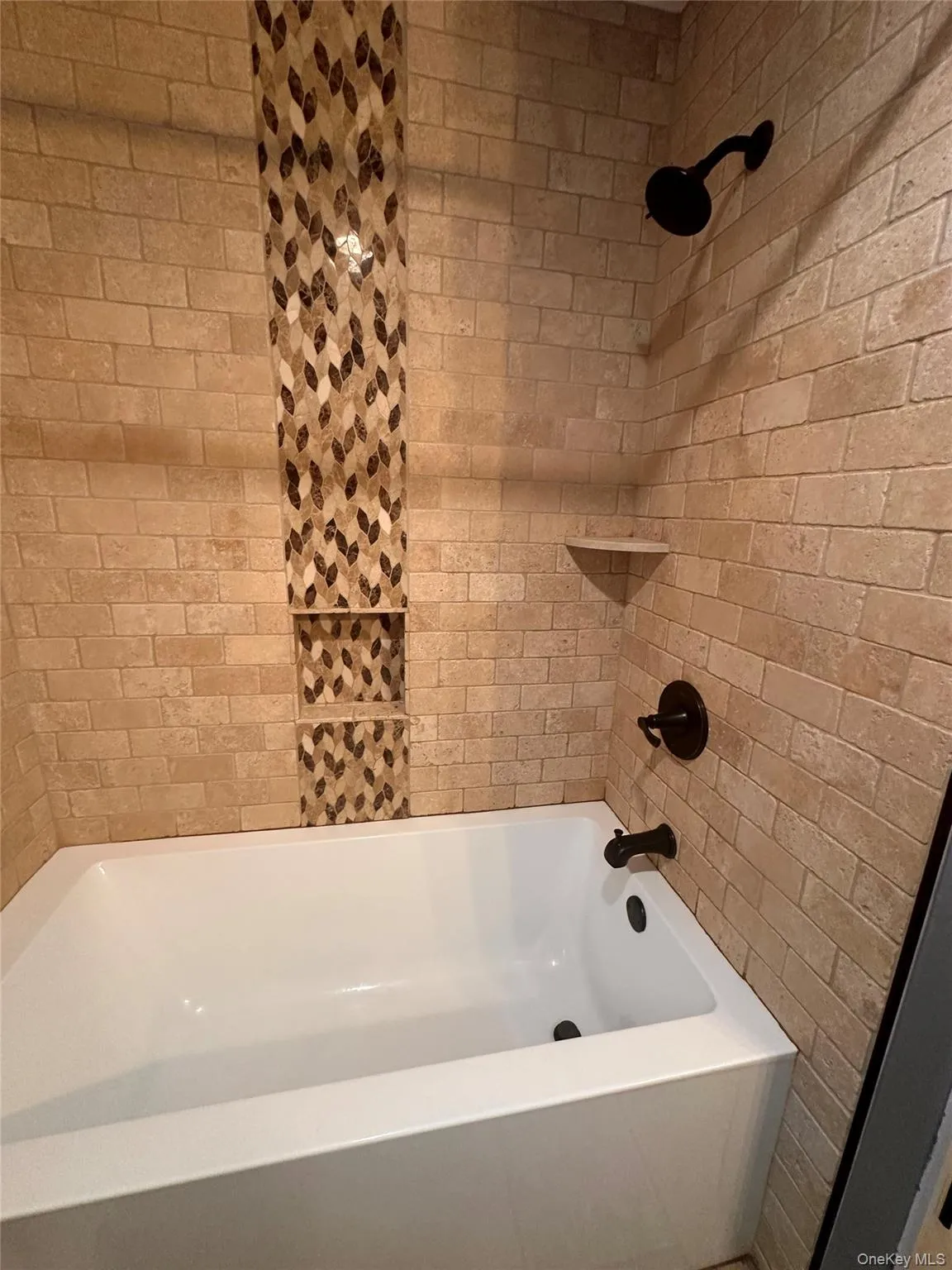 Bathtub and shower surround featuring stacked natural stone tile, a mosaic accent strip, built-in shower niches, and dark bronze fixtures Bathtub and shower surround featuring stacked natural stone tile, a mosaic accent strip, built-in shower niches, and dark bronze fixtures