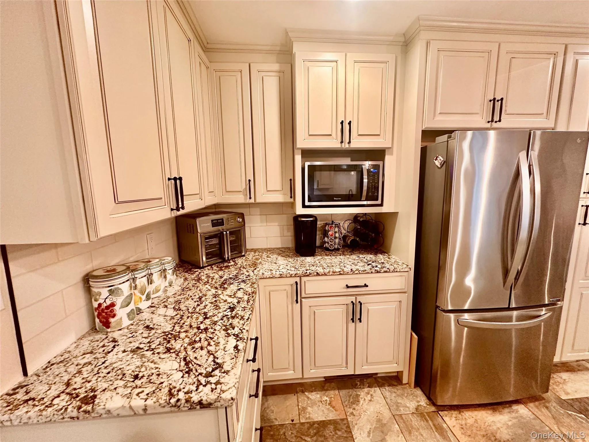 Modern kitchen featuring light-toned cabinetry with dark hardware, speckled countertops, a built-in microwave, and stainless steel appliances Modern kitchen featuring light-toned cabinetry with dark hardware, speckled countertops, a built-in microwave, and stainless steel appliances