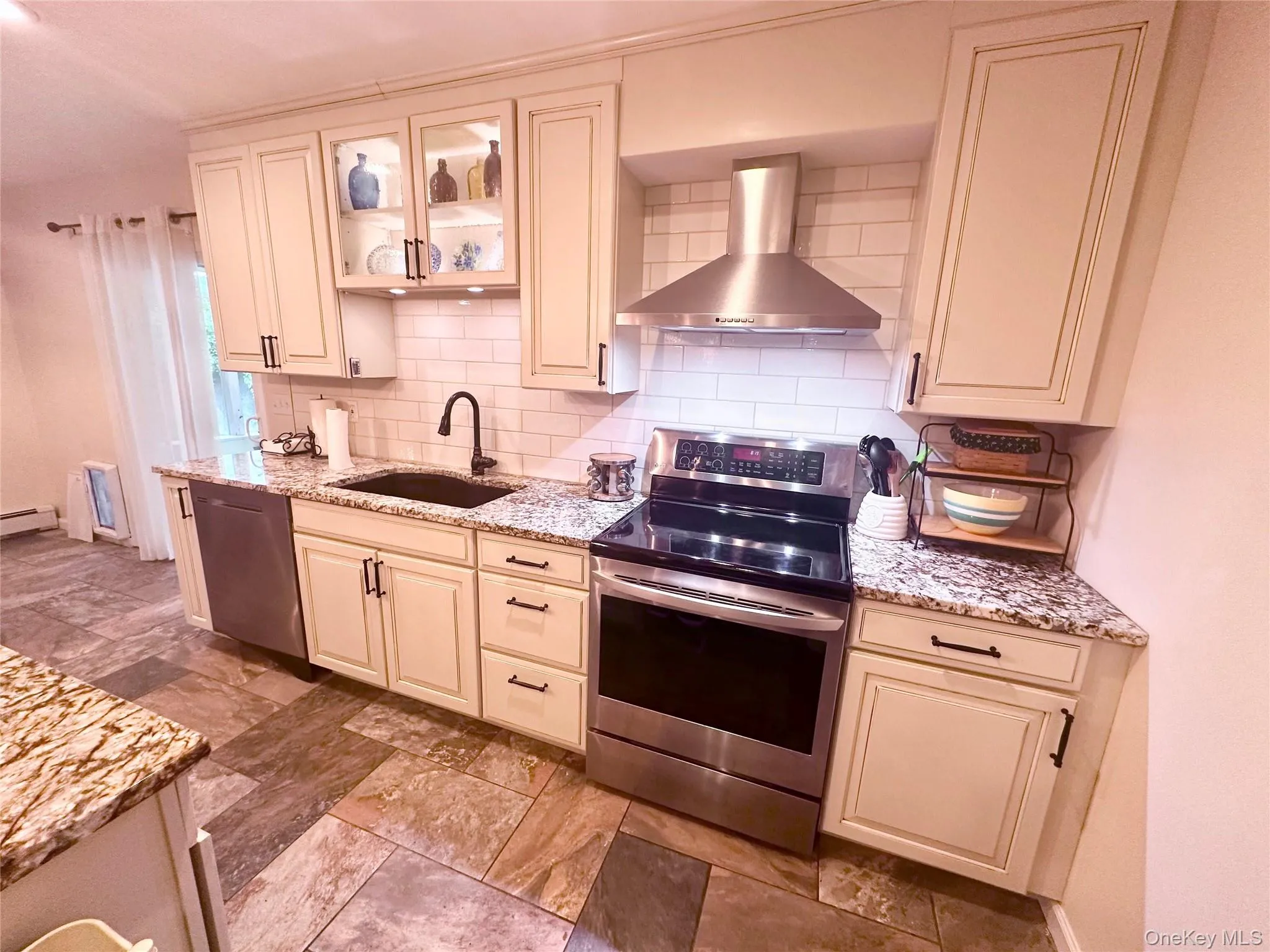 Contemporary kitchen featuring light-toned cabinetry, granite countertops, subway tile backsplash, stainless steel appliances, and multi-toned tile flooring Contemporary kitchen featuring light-toned cabinetry, granite countertops, subway tile backsplash, stainless steel appliances, and multi-toned tile flooring