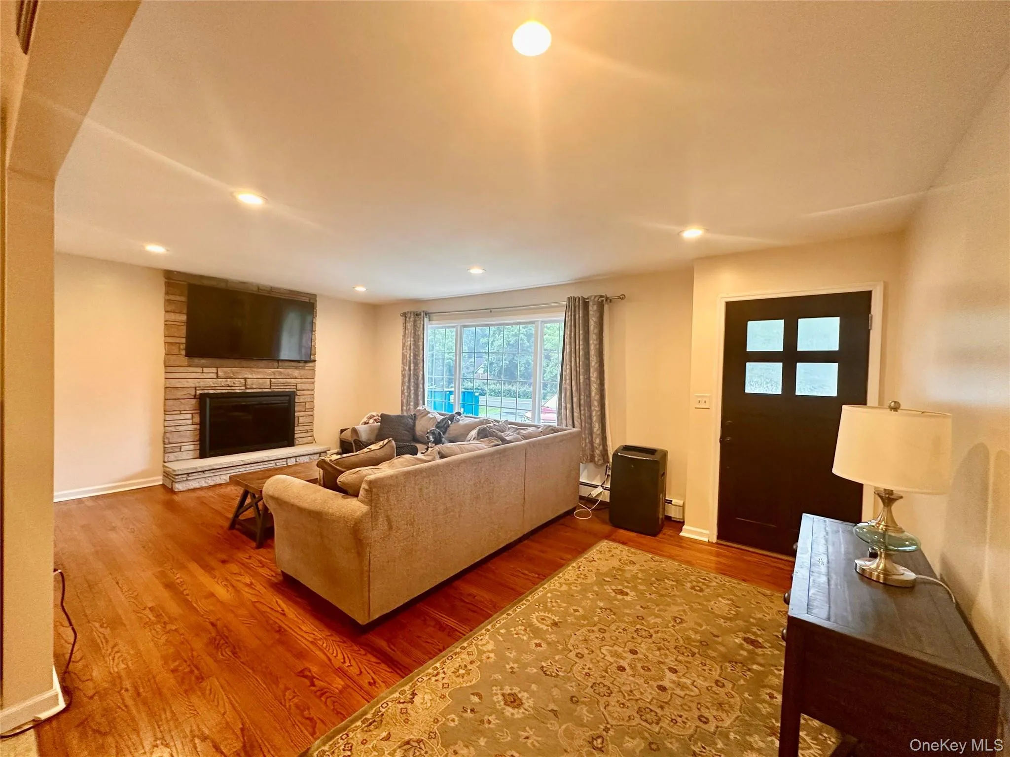 Living area featuring wood-finish flooring, a stone-clad fireplace, and recessed lighting Living area featuring wood-finish flooring, a stone-clad fireplace, and recessed lighting