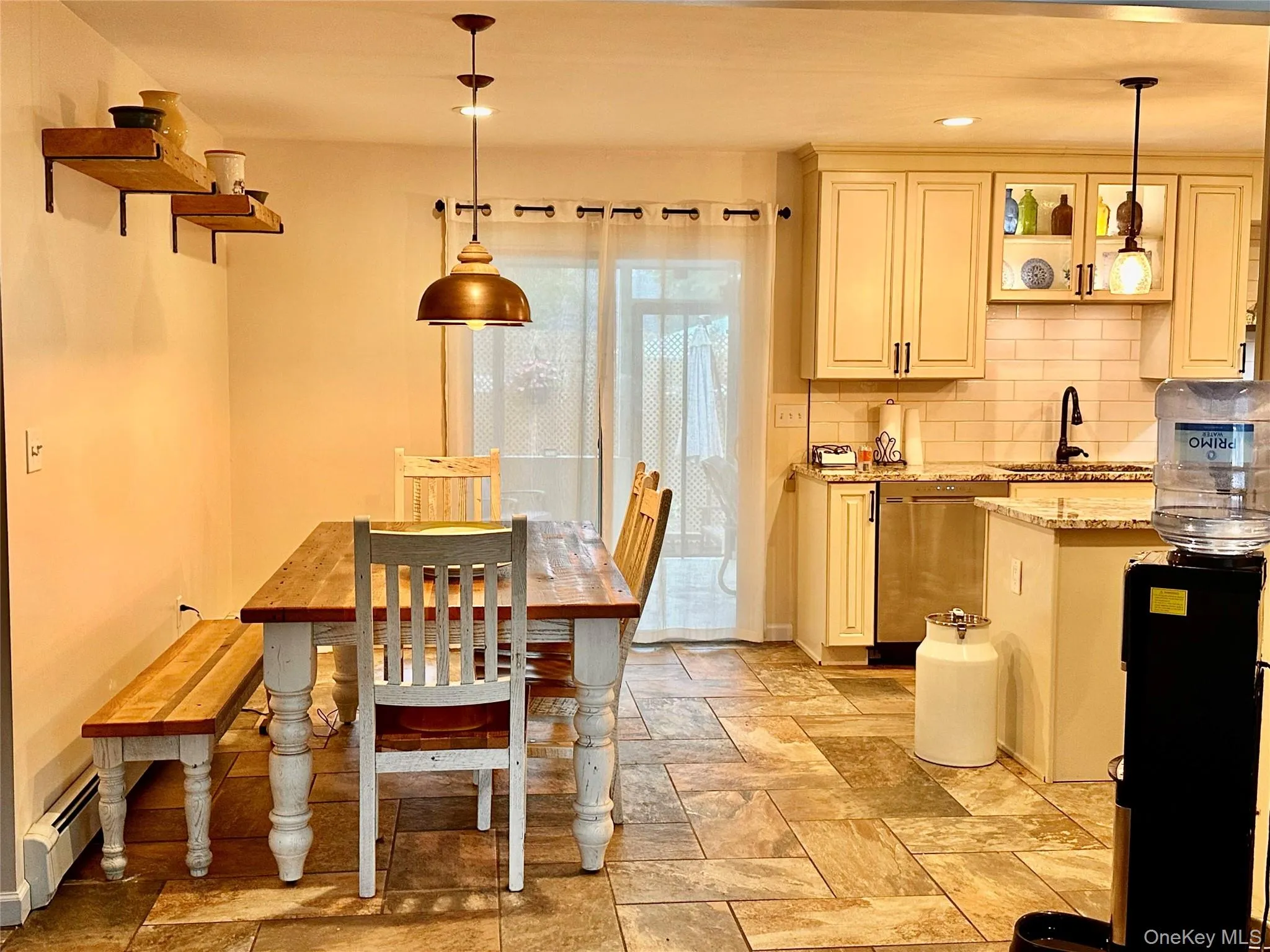 Spacious kitchen and dining area featuring stone tile flooring, cream-colored cabinetry, stainless steel appliances and granite countertops Spacious kitchen and dining area featuring stone tile flooring, cream-colored cabinetry, stainless steel appliances and granite countertops