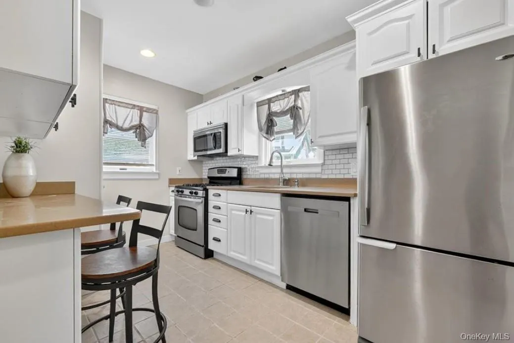 Kitchen with stainless steel appliances, white cabinets, tasteful backsplash, recessed lighting and a breakfast bar Kitchen with stainless steel appliances, white cabinets, tasteful backsplash, recessed lighting and a breakfast bar