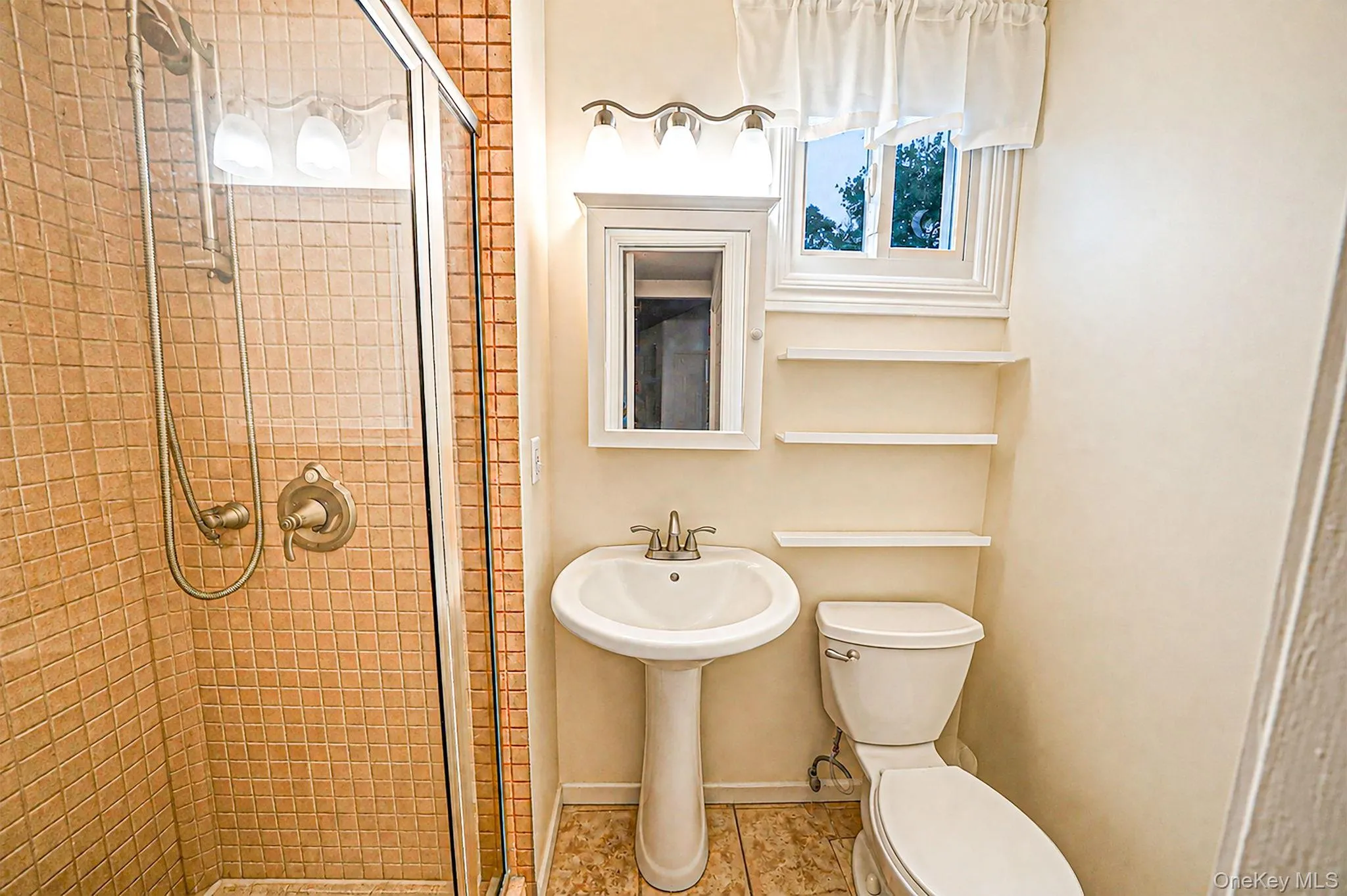 Bathroom featuring a glass-enclosed shower with tile surround, pedestal sink, and built-in shelving Bathroom featuring a glass-enclosed shower with tile surround, pedestal sink, and built-in shelving