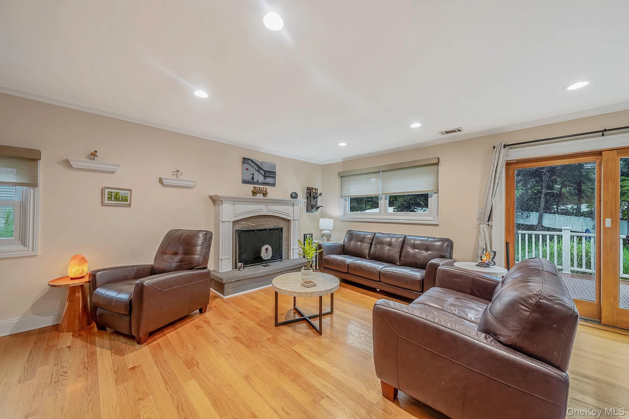 Living room featuring a stone fireplace with hearth, hardwood flooring, recessed lighting, and a glass sliding door leading to an outdoor deck Living room featuring a stone fireplace with hearth, hardwood flooring, recessed lighting, and a glass sliding door leading to an outdoor deck