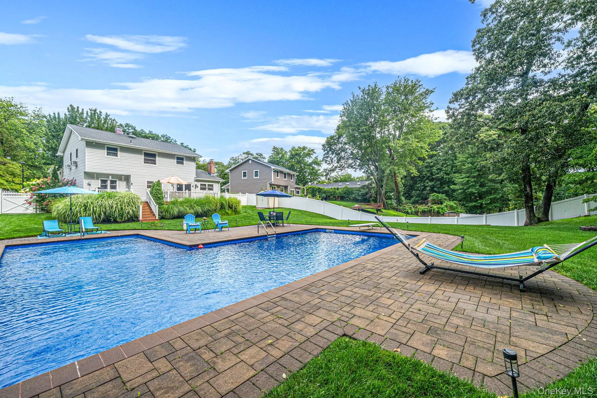 Expansive backyard featuring a large in-ground pool with integrated steps, surrounded by a paver patio Expansive backyard featuring a large in-ground pool with integrated steps, surrounded by a paver patio