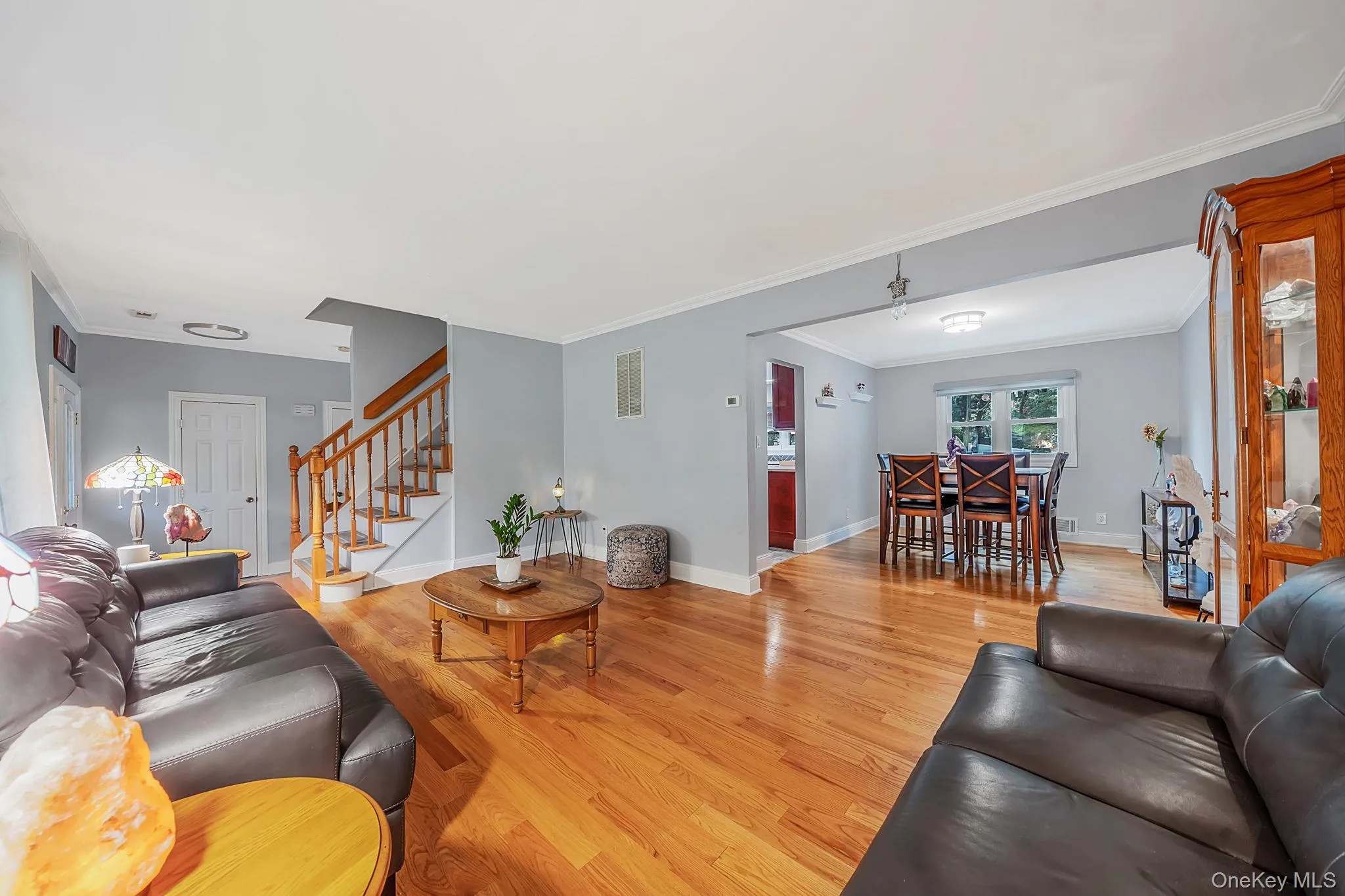 Expansive living area featuring hardwood flooring, light gray wall paint, and white crown molding Expansive living area featuring hardwood flooring, light gray wall paint, and white crown molding