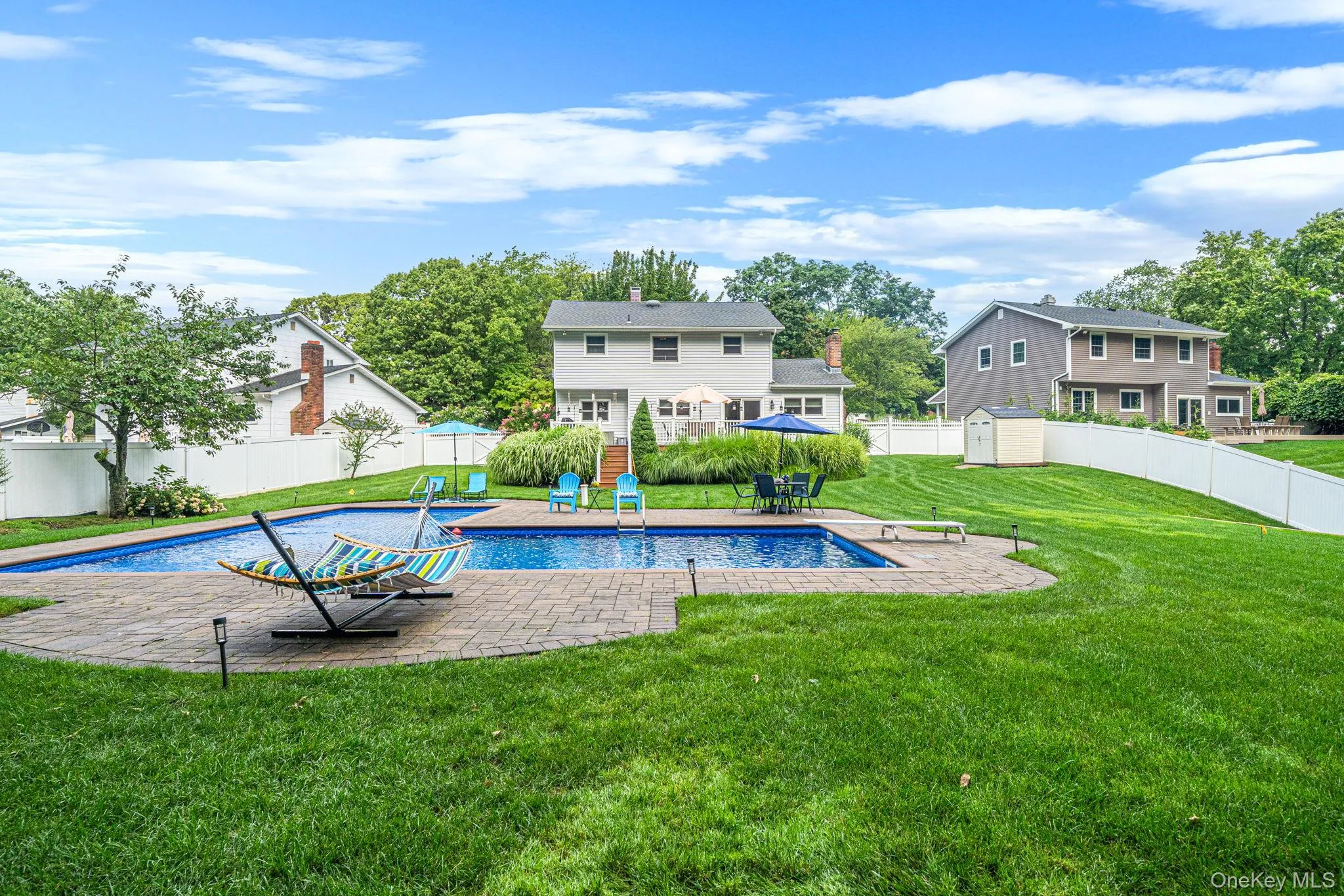 Expansive backyard featuring an in-ground swimming pool with stone paver surround, a white privacy fence, and a detached storage shed Expansive backyard featuring an in-ground swimming pool with stone paver surround, a white privacy fence, and a detached storage shed