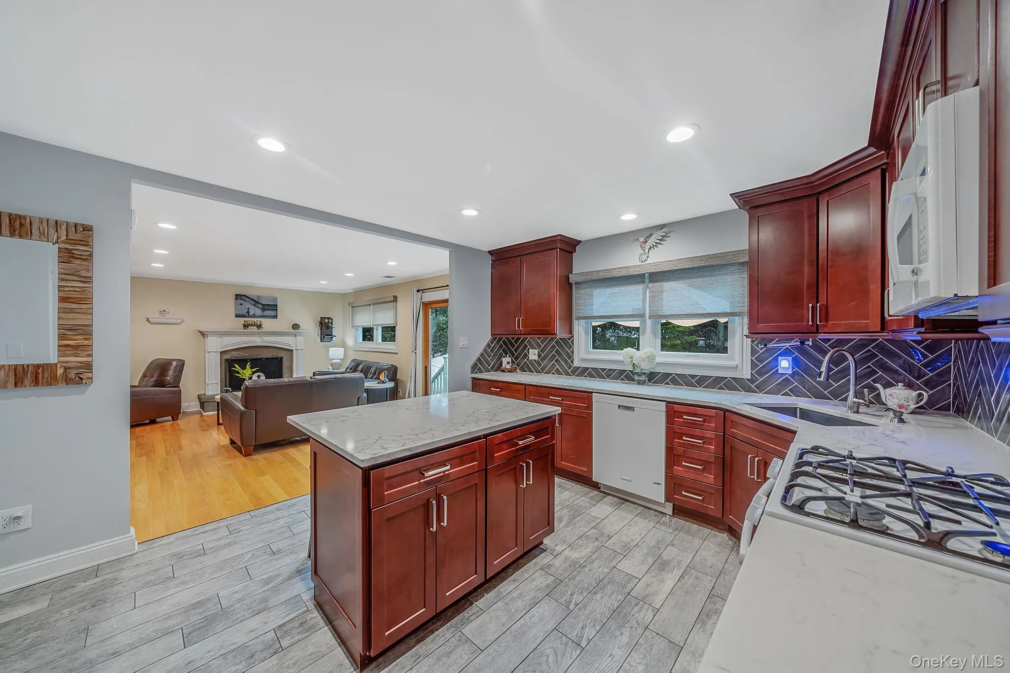 Kitchen featuring cherry-finish cabinetry, light-toned countertops, and a herringbone-patterned tile backsplash Kitchen featuring cherry-finish cabinetry, light-toned countertops, and a herringbone-patterned tile backsplash