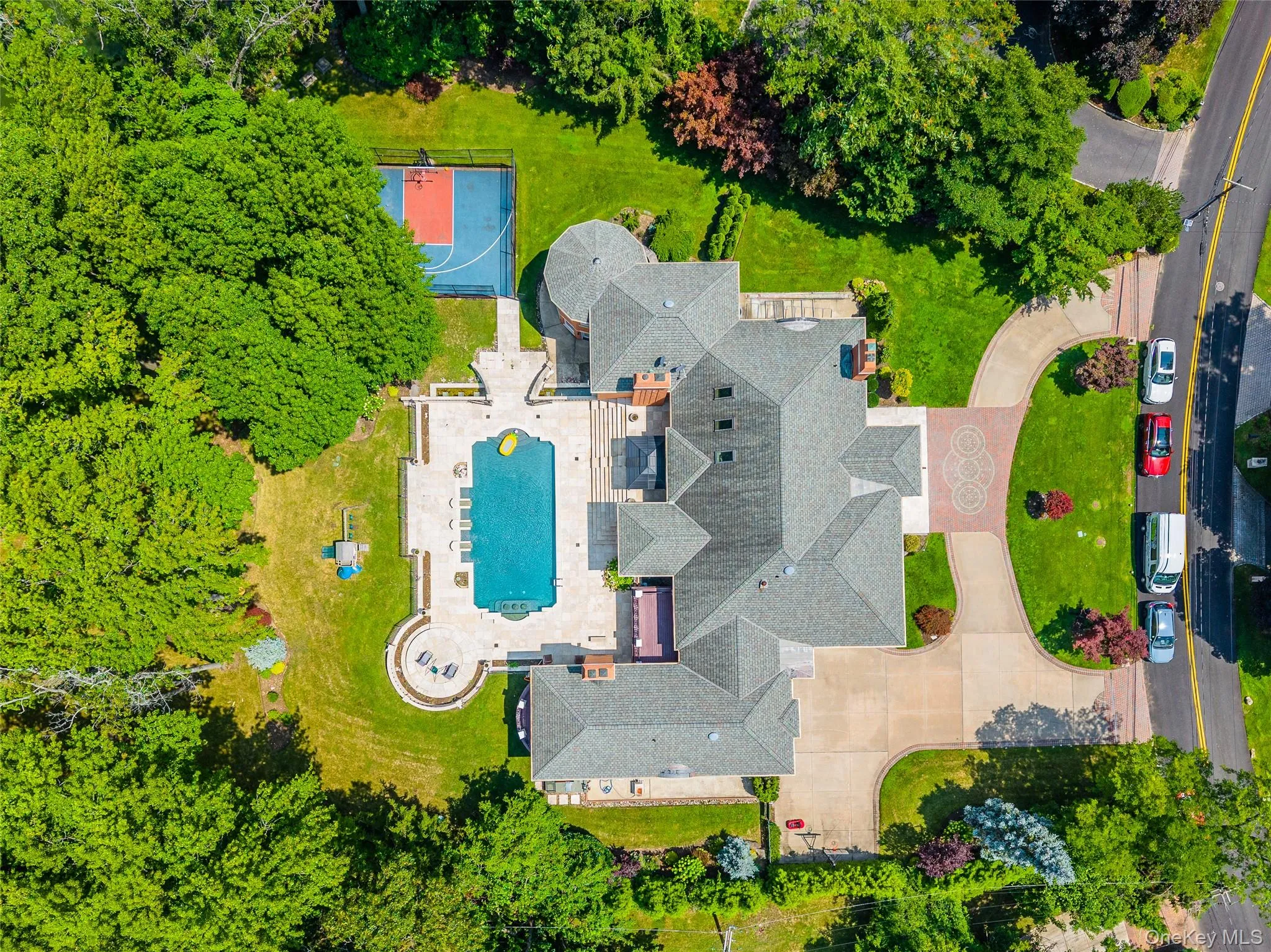 Expansive property featuring a large residence with a multi-level roofline, a winding driveway with paver accents, an integrated swimming pool with a surrounding patio, a dedicated sports court, and mature landscaping Expansive property featuring a large residence with a multi-level roofline, a winding driveway with paver accents, an integrated swimming pool with a surrounding patio, a dedicated sports court, and mature landscaping