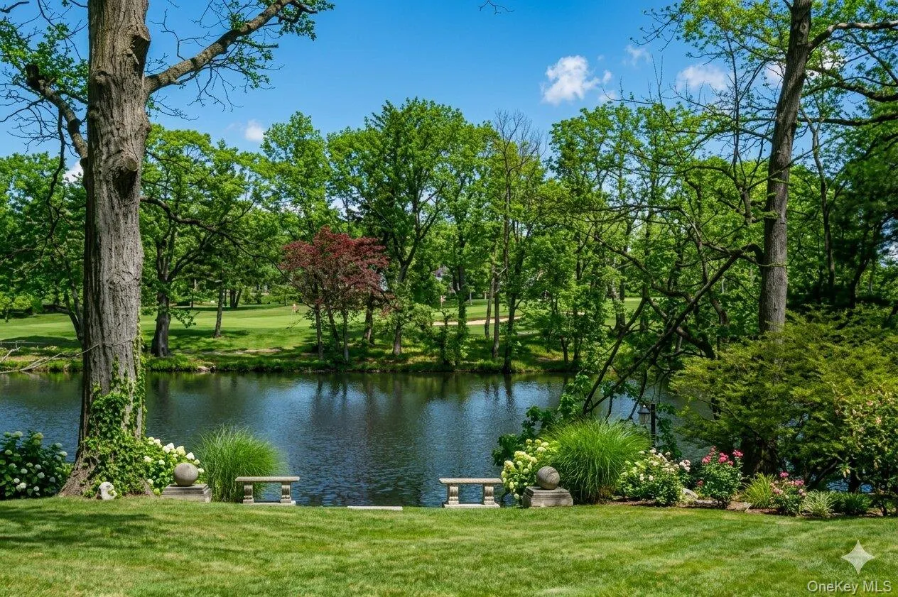 Expansive green lawn bordering a serene body of water, framed by mature trees and lush landscaping Expansive green lawn bordering a serene body of water, framed by mature trees and lush landscaping