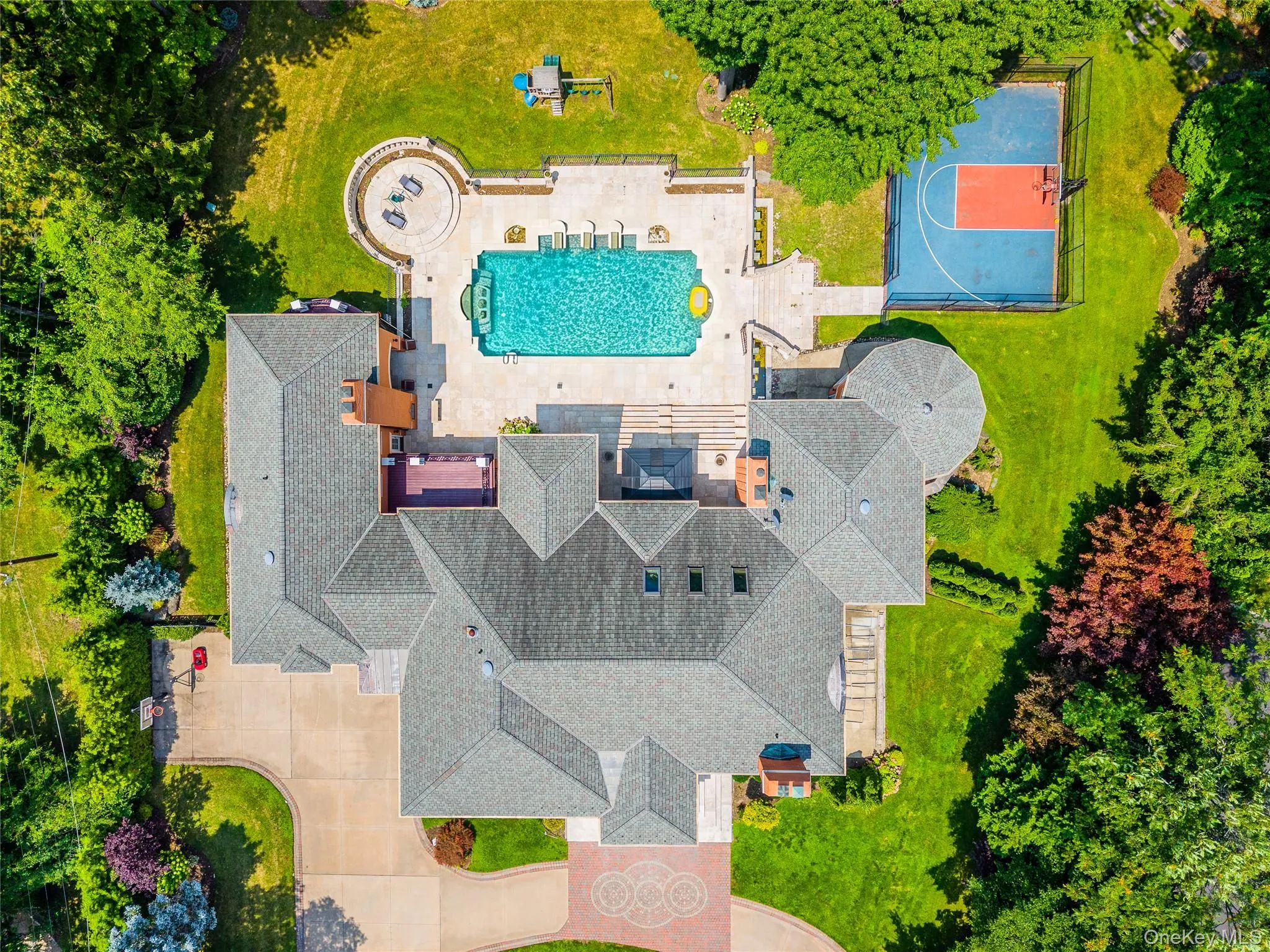 Expansive estate featuring a large swimming pool, paved patio, circular fire pit area, and a private sports court Expansive estate featuring a large swimming pool, paved patio, circular fire pit area, and a private sports court