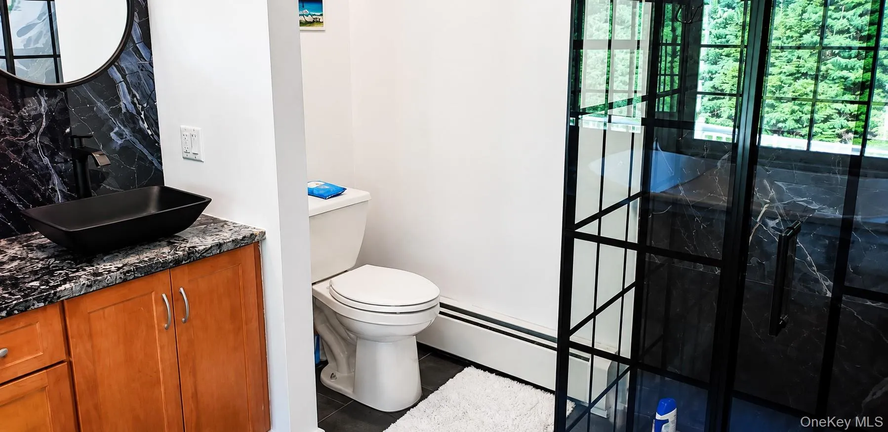 Bathroom featuring a black framed glass shower enclosure, a vessel sink with a matte black faucet, a dark granite-style countertop, and a black circular mirror Bathroom featuring a black framed glass shower enclosure, a vessel sink with a matte black faucet, a dark granite-style countertop, and a black circular mirror