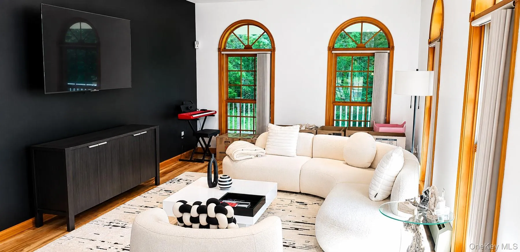 Living space featuring a striking accent wall, light wood-finish flooring, and multiple arched windows with natural wood frames Living space featuring a striking accent wall, light wood-finish flooring, and multiple arched windows with natural wood frames
