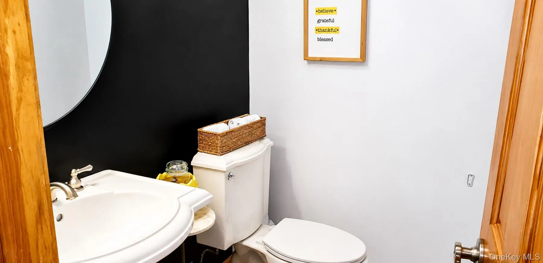 Bathroom featuring a pedestal sink, round mirror, and a toilet Bathroom featuring a pedestal sink, round mirror, and a toilet