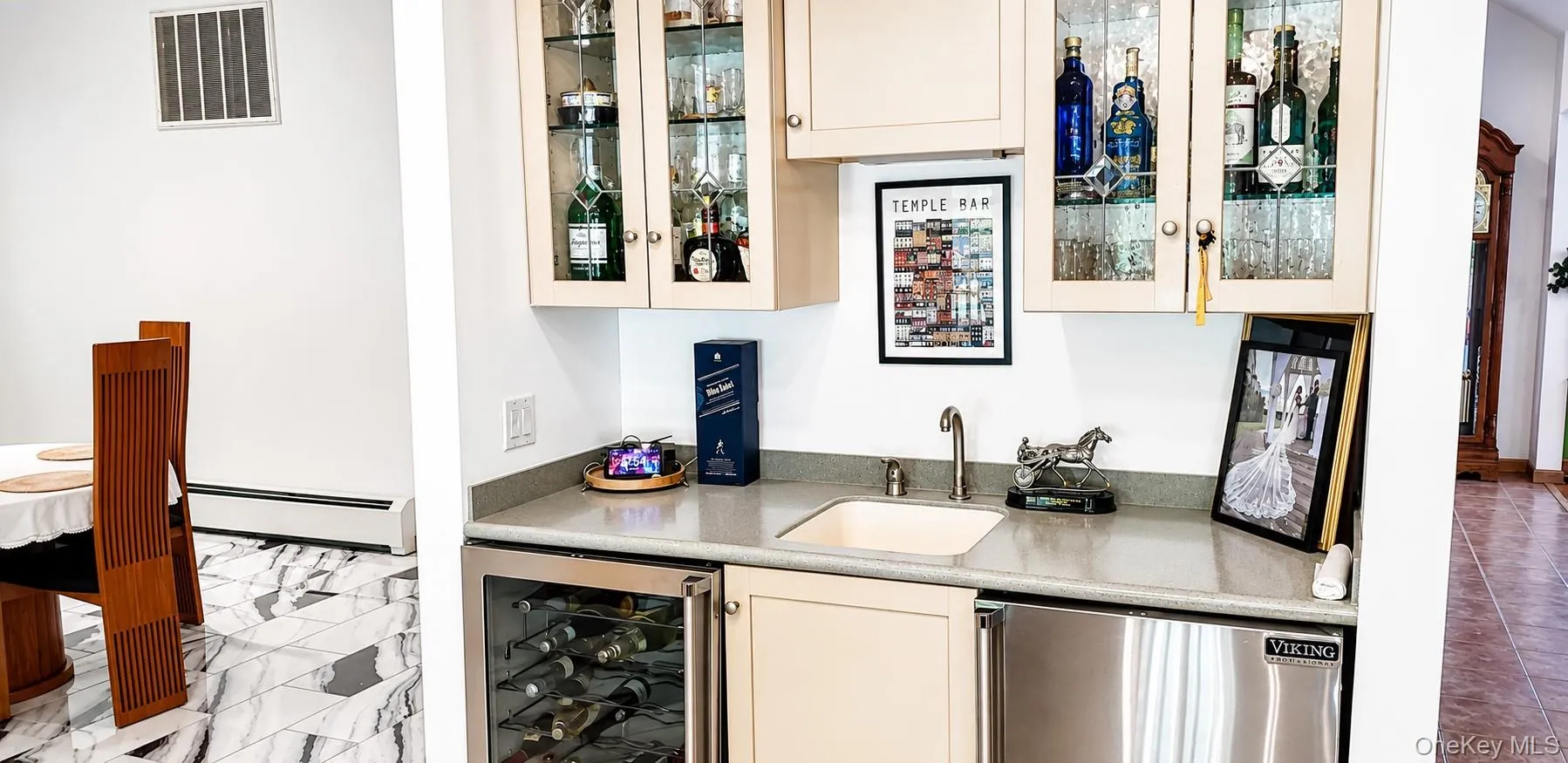 Built-in wet bar featuring upper glass-front cabinetry, a undermount sink with a gooseneck faucet, a wine refrigerator, and a stainless steel undercounter appliance Built-in wet bar featuring upper glass-front cabinetry, a undermount sink with a gooseneck faucet, a wine refrigerator, and a stainless steel undercounter appliance