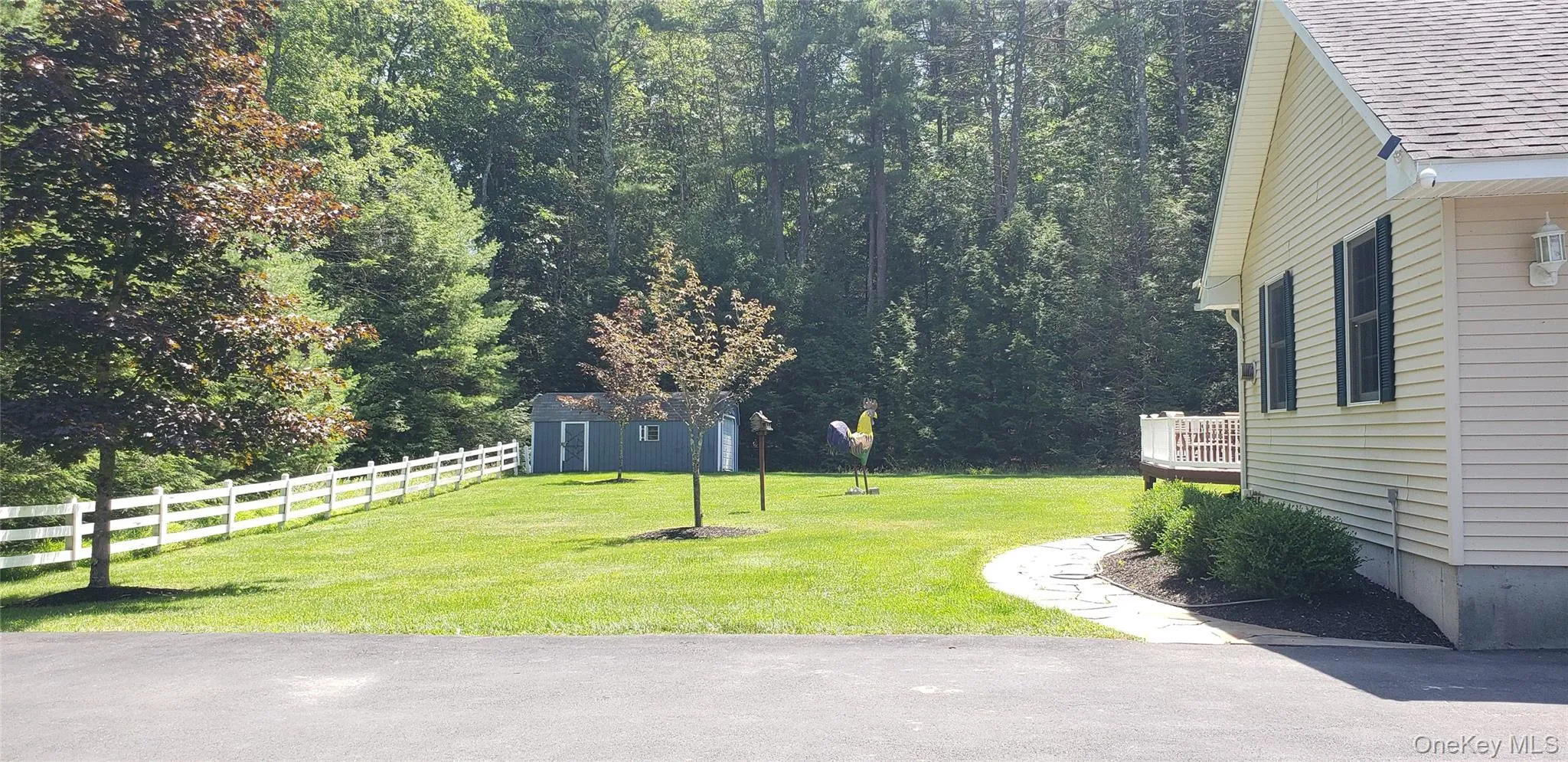 Expansive green lawn framed by mature trees, featuring a white picket fence, a detached storage shed, and a stone pathway leading to the home's exterior Expansive green lawn framed by mature trees, featuring a white picket fence, a detached storage shed, and a stone pathway leading to the home's exterior