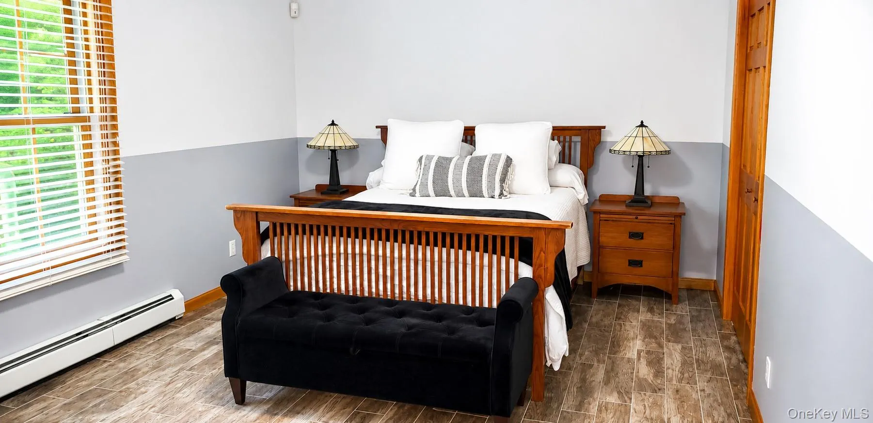 Room featuring wood-finish flooring, a double-hung window with blinds, and a paneled wood door Room featuring wood-finish flooring, a double-hung window with blinds, and a paneled wood door
