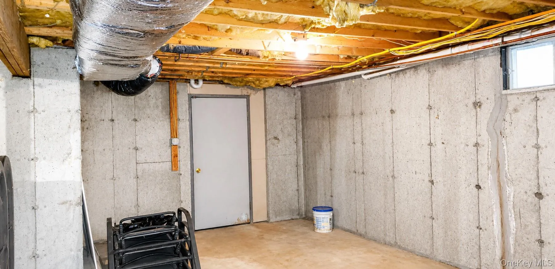 Unfinished basement featuring concrete walls, exposed ceiling joists with insulation, a single window, and a white interior door Unfinished basement featuring concrete walls, exposed ceiling joists with insulation, a single window, and a white interior door