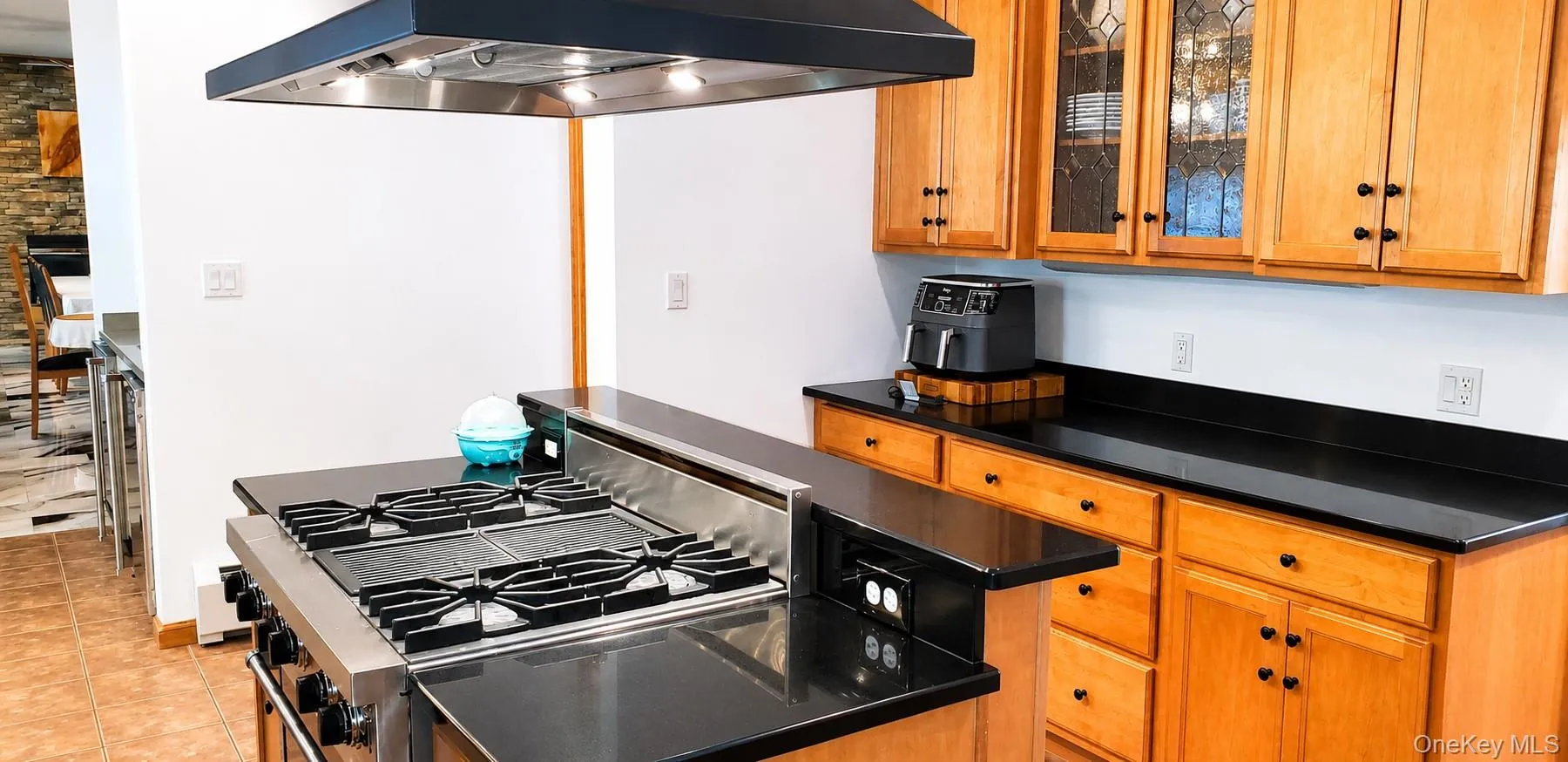 Professional-grade stainless steel range with overhead ventilation hood, complemented by black countertops and light wood-finish cabinetry Professional-grade stainless steel range with overhead ventilation hood, complemented by black countertops and light wood-finish cabinetry