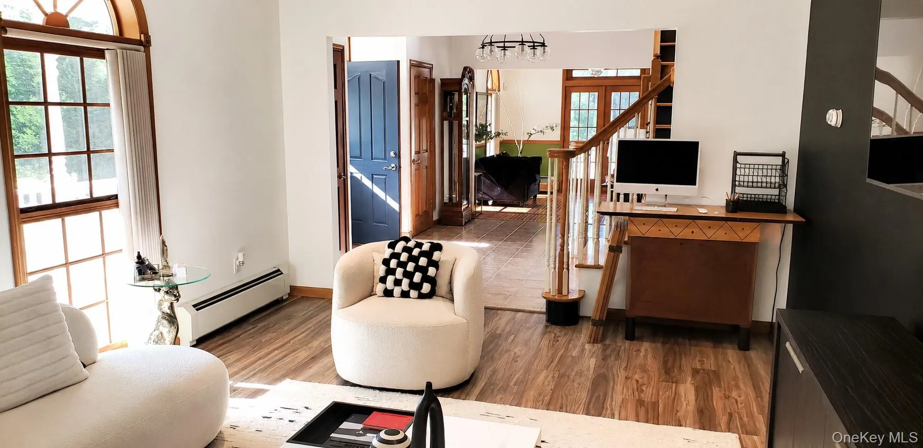 Spacious living area featuring wood-finish flooring, an arched window, and bright white walls Spacious living area featuring wood-finish flooring, an arched window, and bright white walls