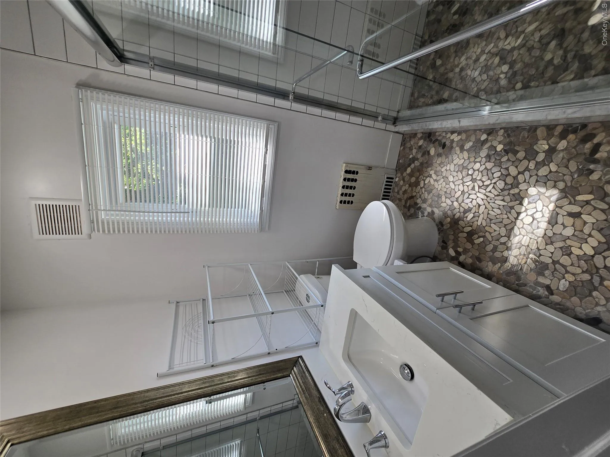 Bathroom featuring a pebble-tile floor, white vanity with integrated sink, chrome faucet, and a glass-enclosed shower Bathroom featuring a pebble-tile floor, white vanity with integrated sink, chrome faucet, and a glass-enclosed shower