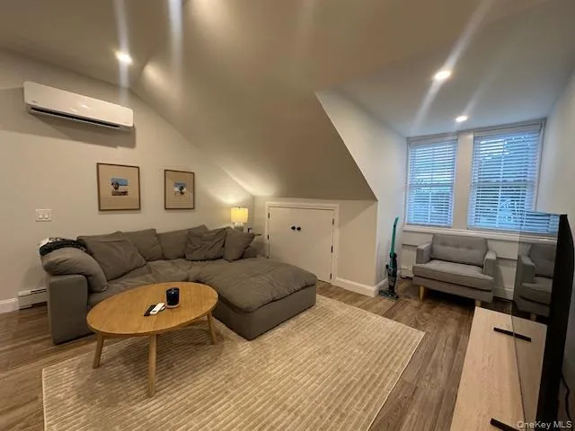 Living room with wood finished floors, an AC wall unit, baseboard heating, lofted ceiling, and recessed lighting Living room with wood finished floors, an AC wall unit, baseboard heating, lofted ceiling, and recessed lighting