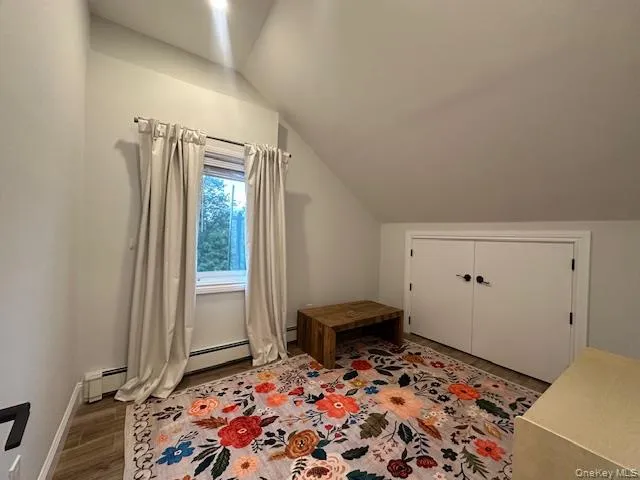 Bonus room featuring wood finished floors, lofted ceiling, and a baseboard heating unit Bonus room featuring wood finished floors, lofted ceiling, and a baseboard heating unit