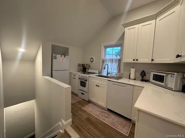 Kitchen with white appliances, white cabinetry, dark wood-style flooring, lofted ceiling, and light stone countertops Kitchen with white appliances, white cabinetry, dark wood-style flooring, lofted ceiling, and light stone countertops