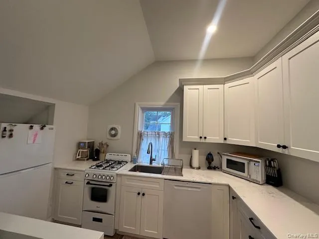 Kitchen featuring white appliances, white cabinets, vaulted ceiling, and light stone countertops Kitchen featuring white appliances, white cabinets, vaulted ceiling, and light stone countertops