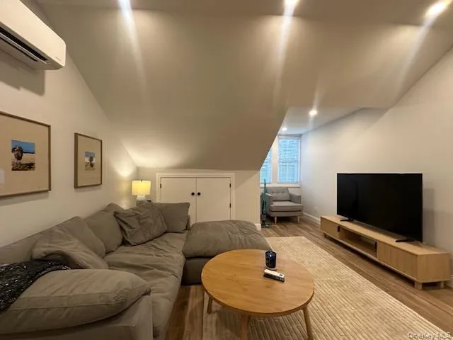 Living room with lofted ceiling, a wall mounted air conditioner, and wood finished floors Living room with lofted ceiling, a wall mounted air conditioner, and wood finished floors