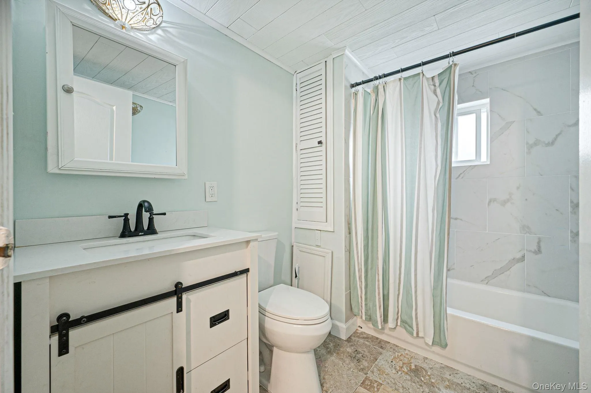 Bathroom featuring a white vanity with barn door style cabinetry, a white countertop with an integrated sink, and a black faucet Bathroom featuring a white vanity with barn door style cabinetry, a white countertop with an integrated sink, and a black faucet