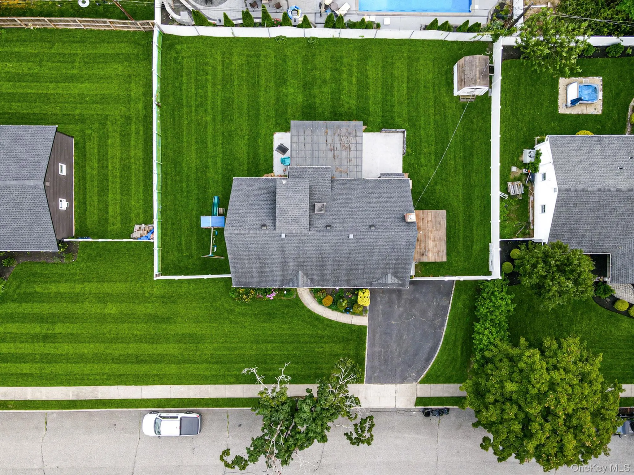 Overhead property view featuring a shingle roof, paved driveway, expansive green lawn, and a rear patio space Overhead property view featuring a shingle roof, paved driveway, expansive green lawn, and a rear patio space