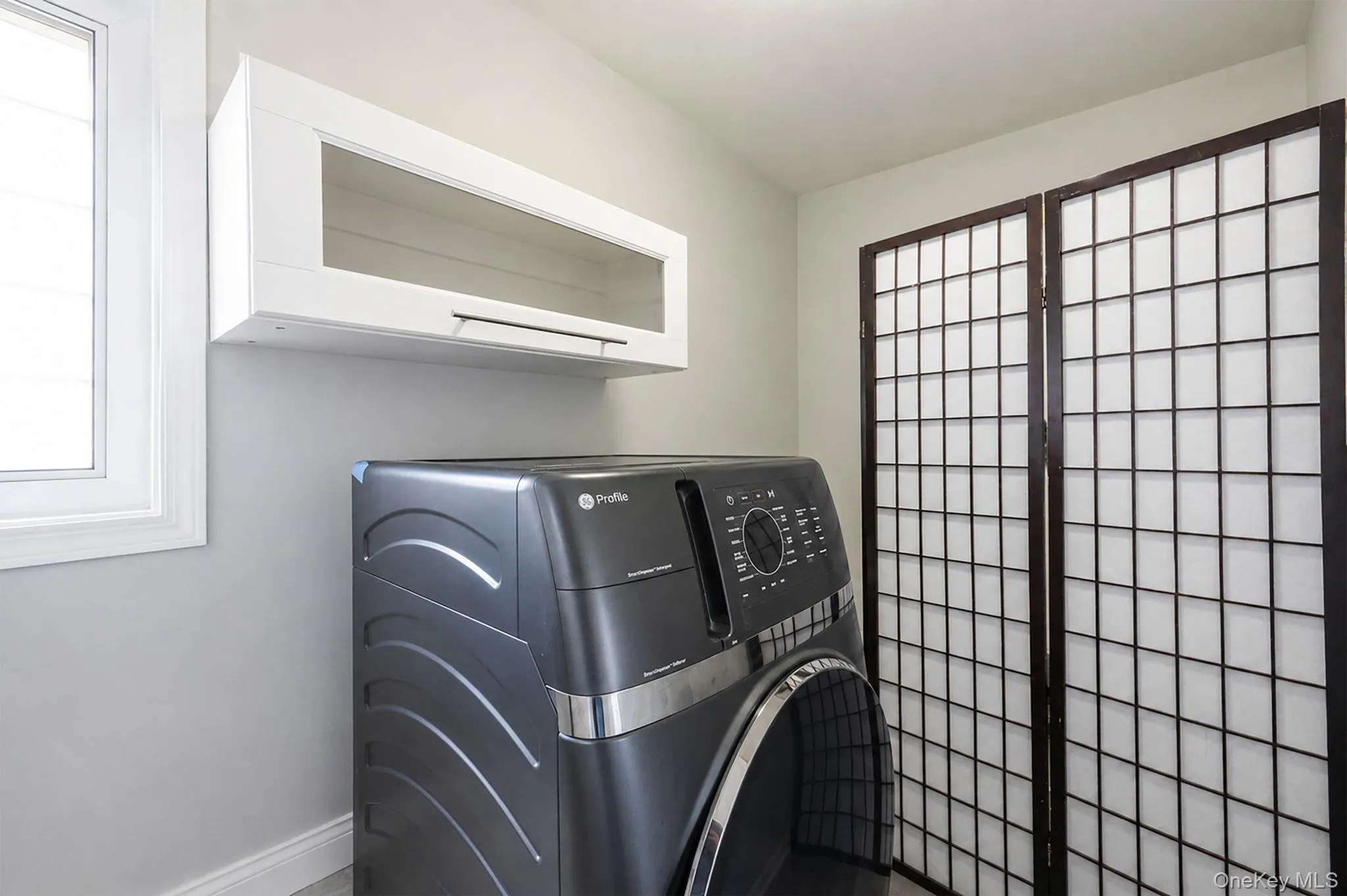 White wall-mounted cabinetry with glass inserts, a single-pane window, light gray wall paint, and dark wood-framed shoji screens White wall-mounted cabinetry with glass inserts, a single-pane window, light gray wall paint, and dark wood-framed shoji screens