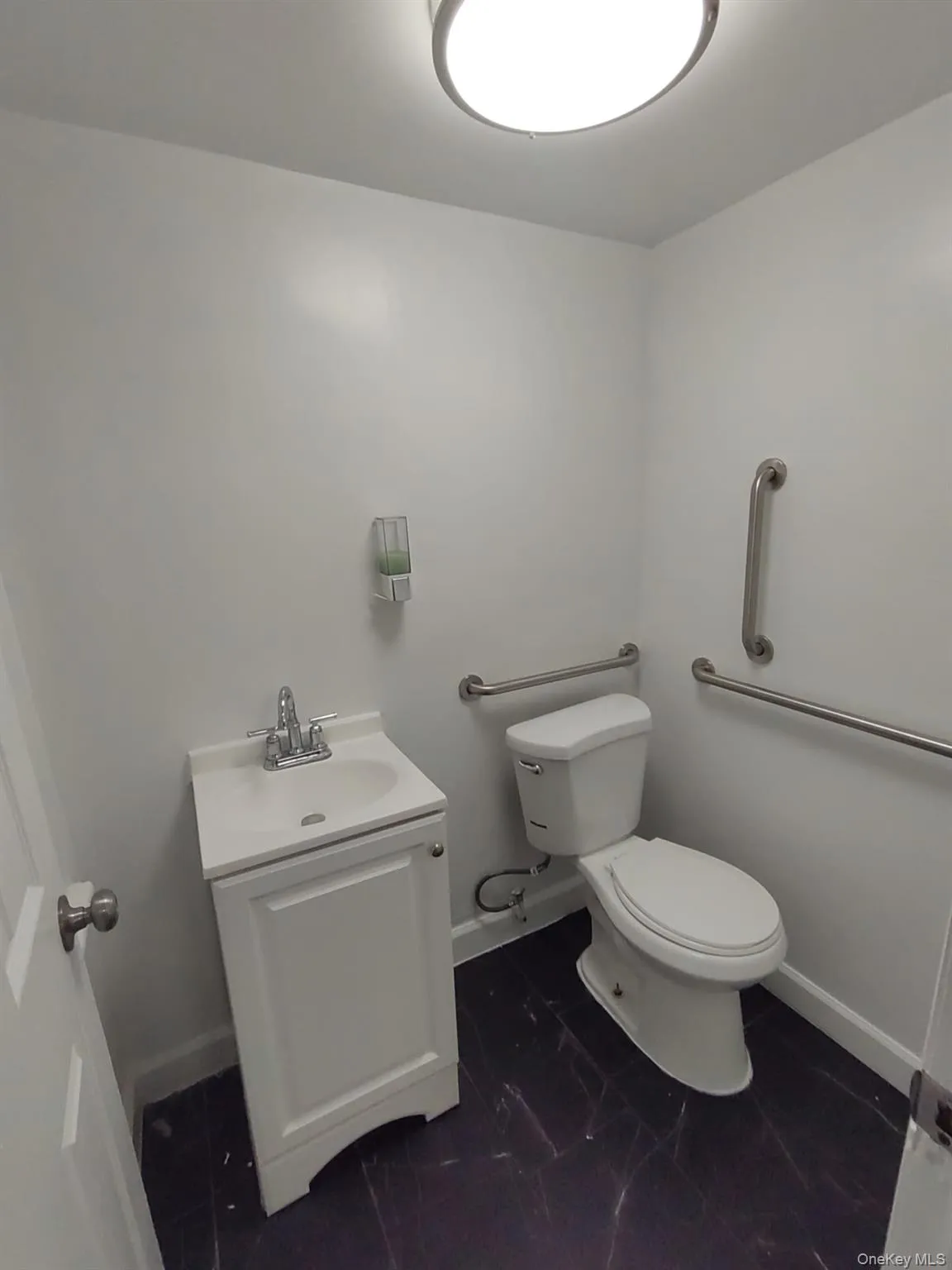 Compact bathroom featuring a white vanity with integrated sink, chrome faucet, and contrasting dark flooring Compact bathroom featuring a white vanity with integrated sink, chrome faucet, and contrasting dark flooring