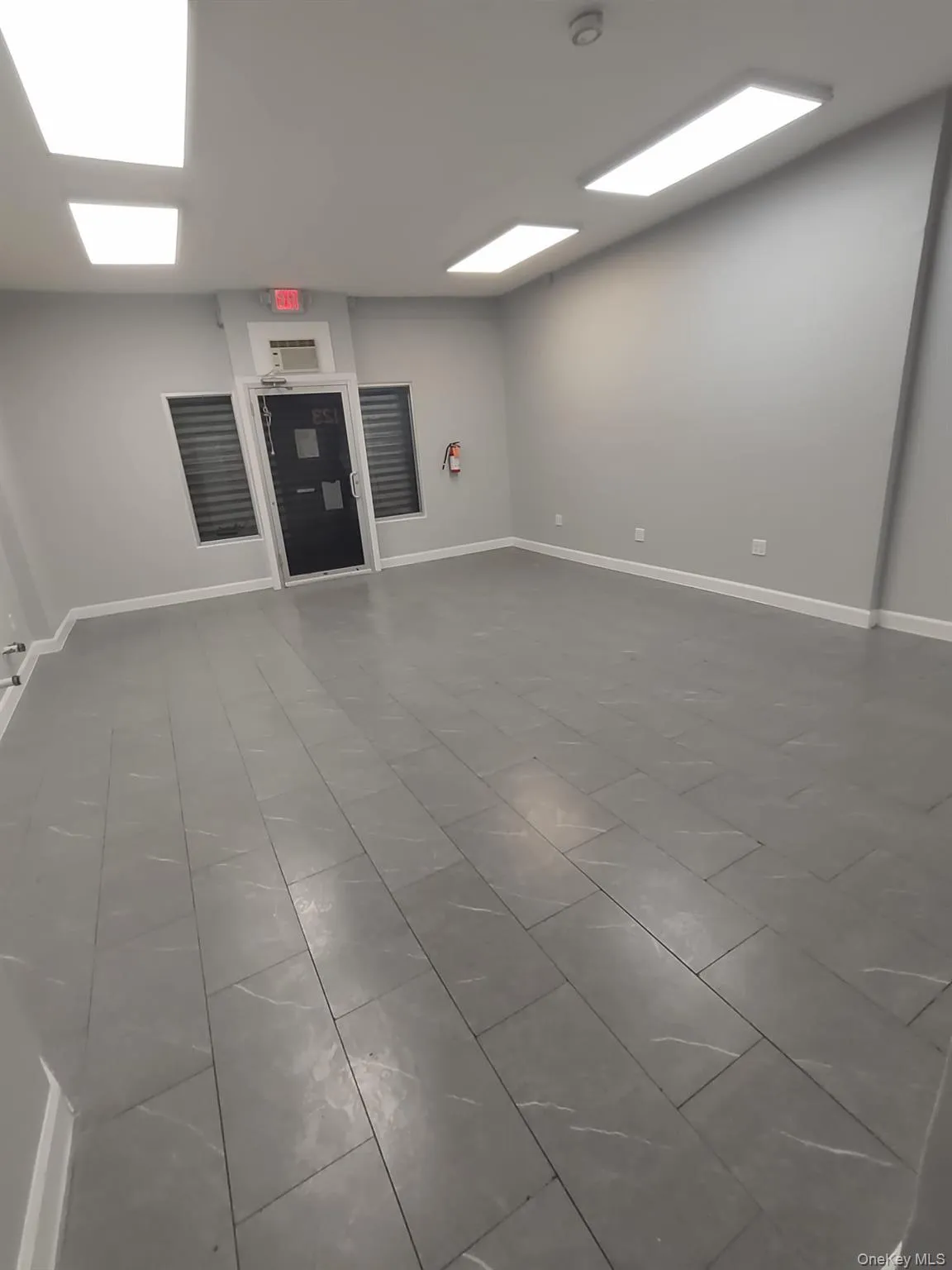 Spacious room featuring large format grey tile flooring, light grey painted walls, and rectangular recessed lighting fixtures Spacious room featuring large format grey tile flooring, light grey painted walls, and rectangular recessed lighting fixtures