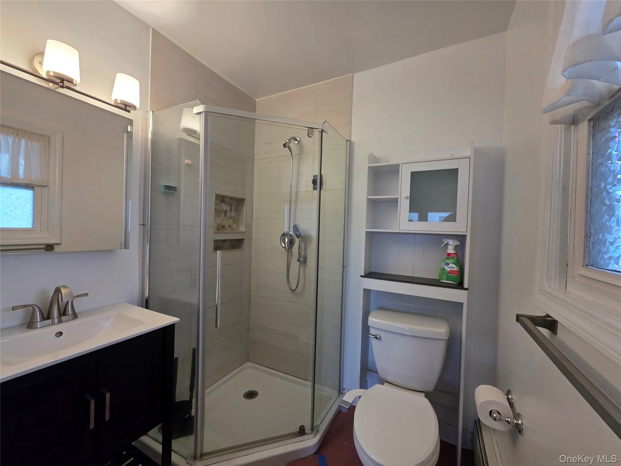 Glass-enclosed shower with tiled surround, single vanity with integrated sink, brushed nickel faucet, and wall-mounted vanity lighting Glass-enclosed shower with tiled surround, single vanity with integrated sink, brushed nickel faucet, and wall-mounted vanity lighting