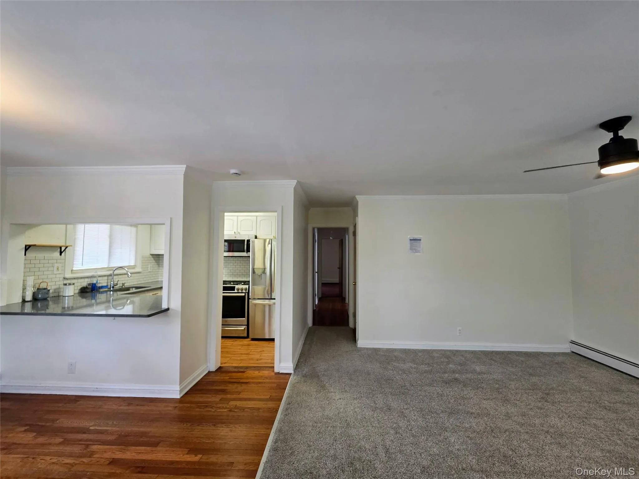 Open-concept living area featuring a pass-through kitchen with dark countertops, white cabinetry, and stainless steel appliances Open-concept living area featuring a pass-through kitchen with dark countertops, white cabinetry, and stainless steel appliances