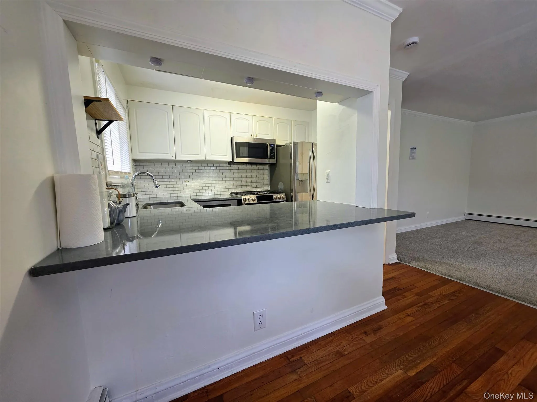Kitchen featuring white cabinetry, stainless steel appliances, a subway tile backsplash, and a breakfast bar with a dark countertop Kitchen featuring white cabinetry, stainless steel appliances, a subway tile backsplash, and a breakfast bar with a dark countertop