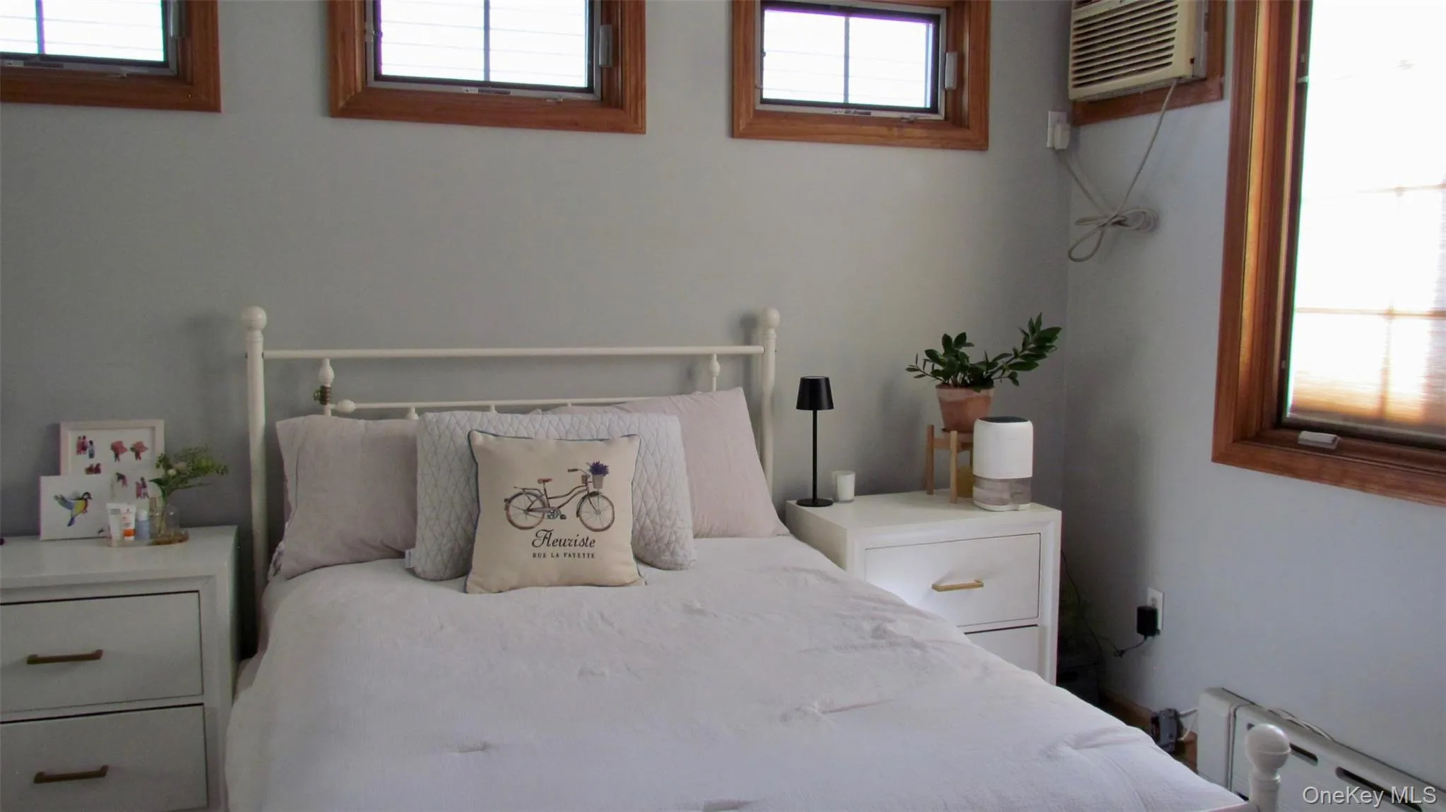 Bedroom featuring light gray walls, multiple windows with wood frames, and a built-in air conditioning unit Bedroom featuring light gray walls, multiple windows with wood frames, and a built-in air conditioning unit