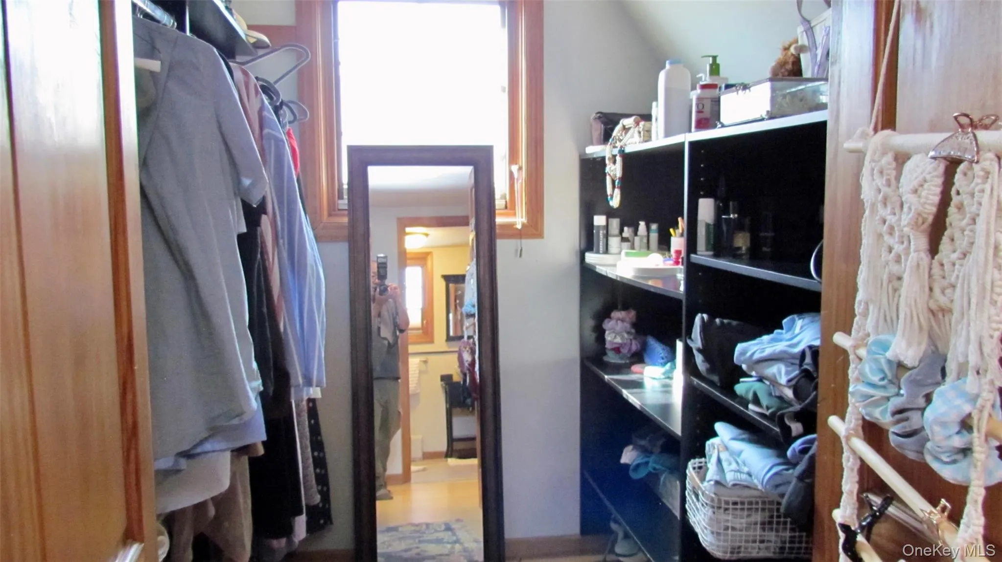 Dedicated walk-in closet space featuring a built-in shelving unit, natural wood trim around a window, and a wood-finish door frame Dedicated walk-in closet space featuring a built-in shelving unit, natural wood trim around a window, and a wood-finish door frame