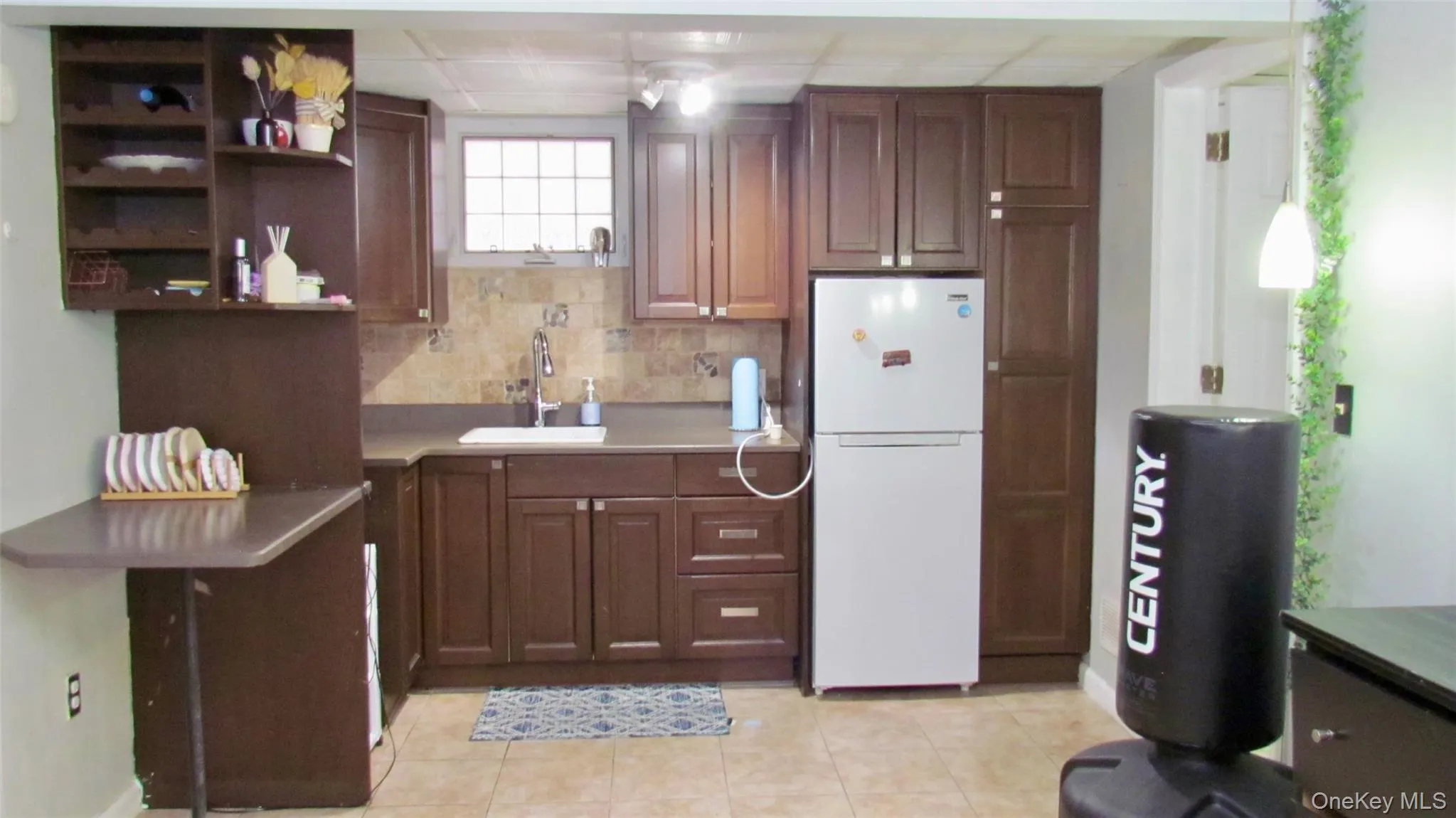 Wood-finish cabinetry, a white basin sink, and a tiled backsplash Wood-finish cabinetry, a white basin sink, and a tiled backsplash