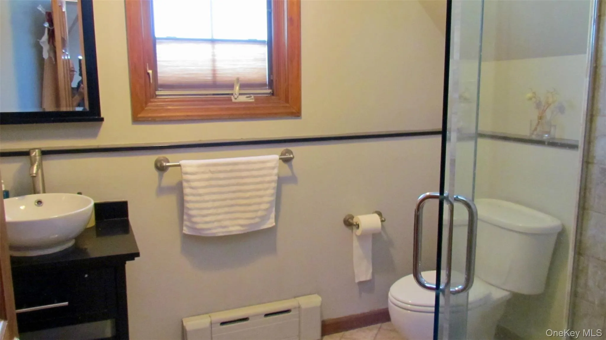 Bathroom featuring a frameless glass shower enclosure, wood-trimmed window, black vanity with vessel sink, and wall-mounted mirror Bathroom featuring a frameless glass shower enclosure, wood-trimmed window, black vanity with vessel sink, and wall-mounted mirror