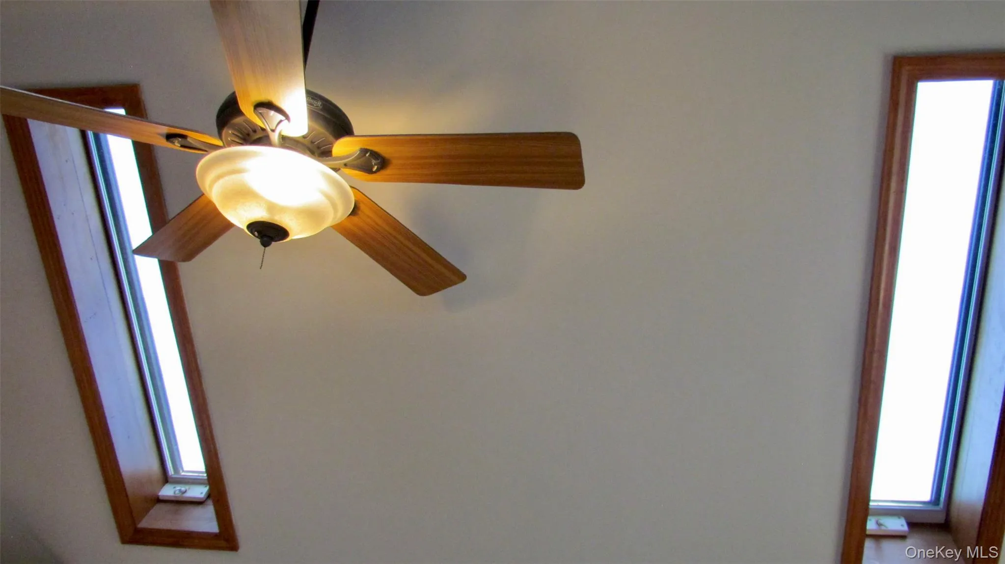 Ceiling fan with light fixture and wood-finish blades, flanked by two elongated skylights with wood trim Ceiling fan with light fixture and wood-finish blades, flanked by two elongated skylights with wood trim