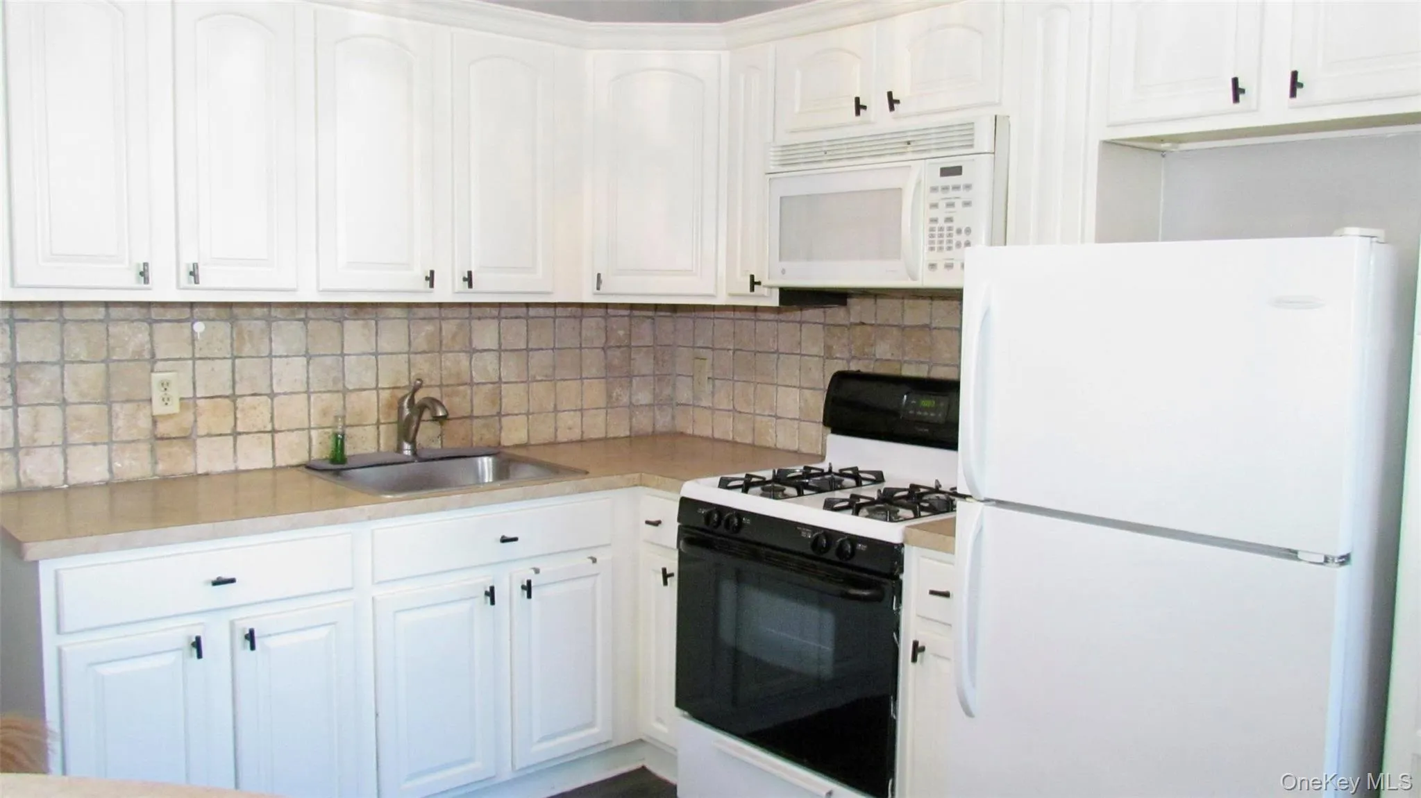 Kitchen featuring white cabinetry, light-toned countertops, a square tile backsplash, and a stainless steel sink Kitchen featuring white cabinetry, light-toned countertops, a square tile backsplash, and a stainless steel sink