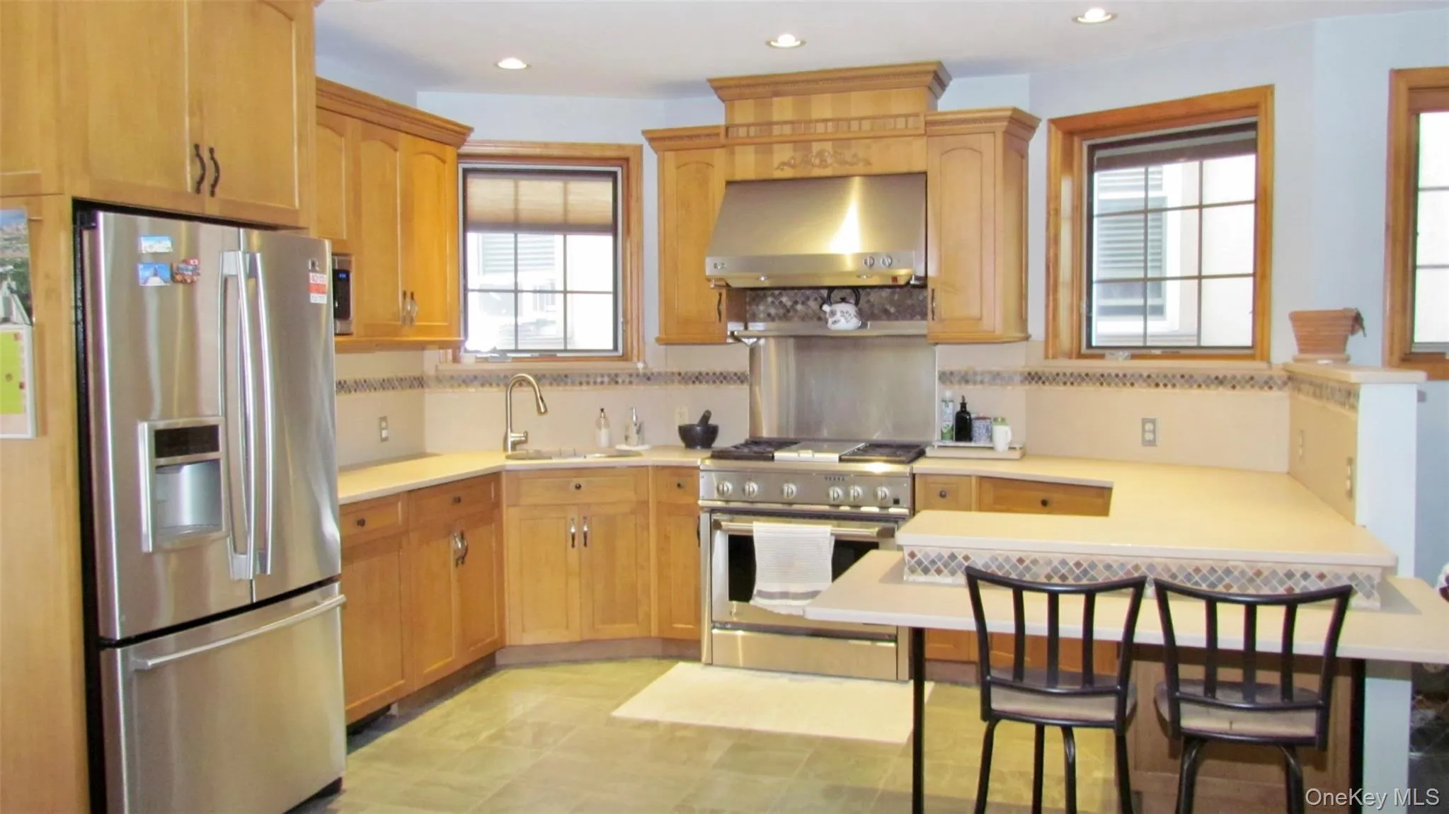 Full kitchen featuring stainless steel appliances, custom wood cabinetry, extensive countertop space, recessed lighting, and tile flooring Full kitchen featuring stainless steel appliances, custom wood cabinetry, extensive countertop space, recessed lighting, and tile flooring