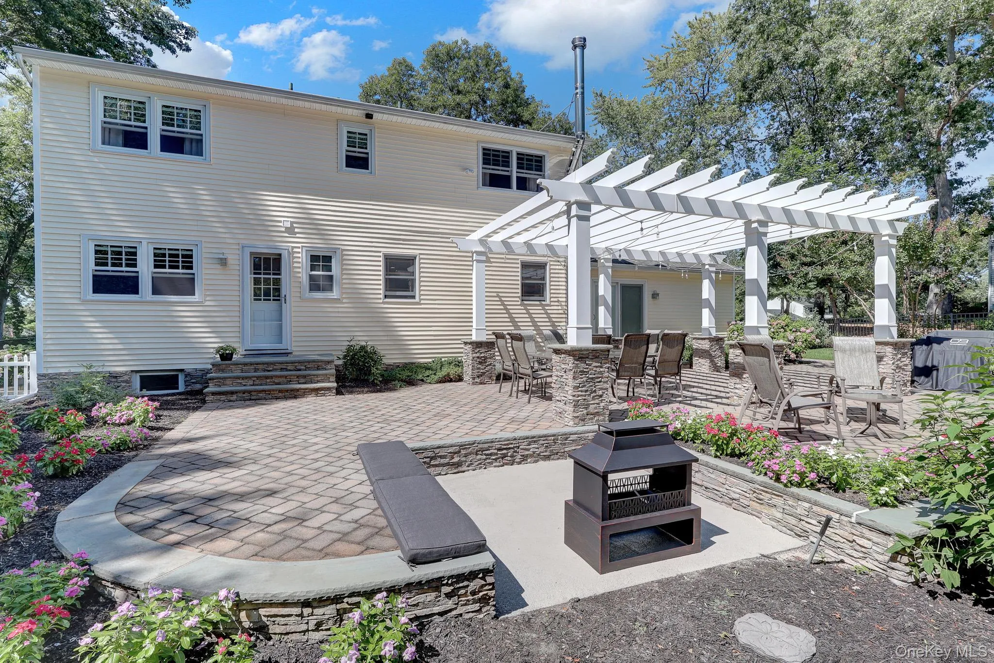 Expansive paver patio with a white pergola, stone-clad pillars, and integrated lighting and fire pit area. Expansive paver patio with a white pergola, stone-clad pillars, and integrated lighting and fire pit area.