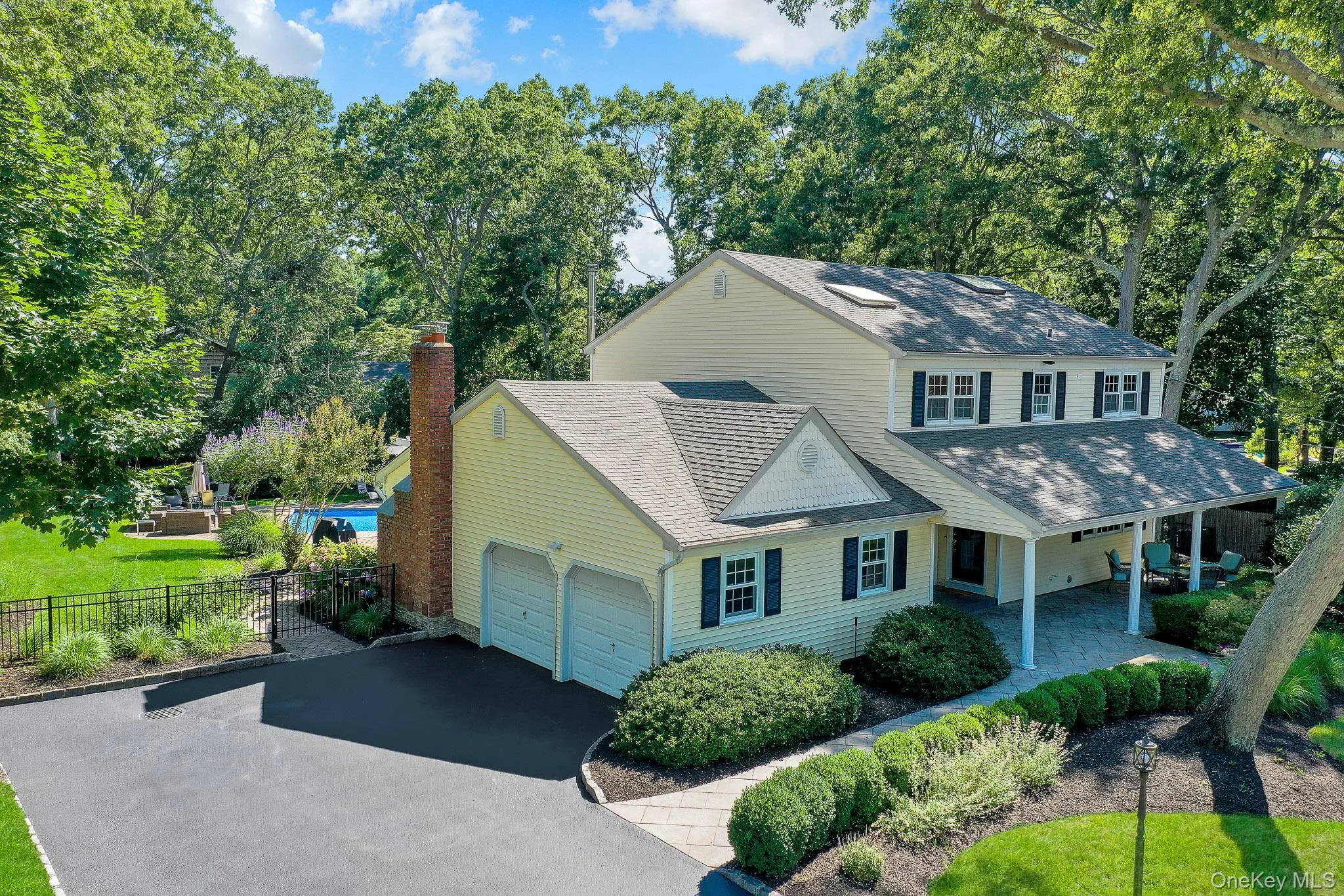 Two-story residence featuring light yellow siding, dark shutters, and a covered front patio with a stone paver surface Two-story residence featuring light yellow siding, dark shutters, and a covered front patio with a stone paver surface
