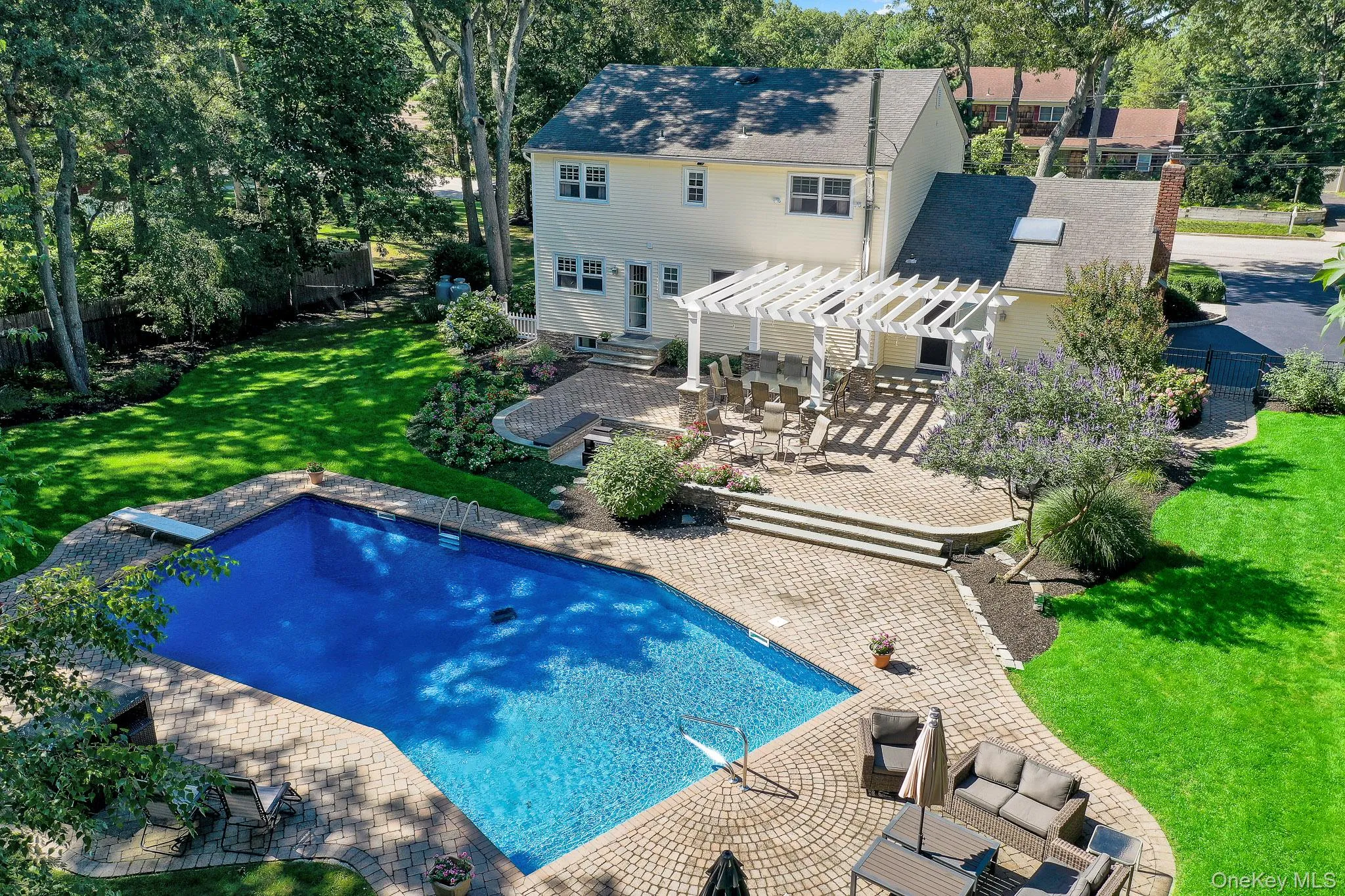 Expansive backyard featuring a large in-ground pool with a diving board, a spacious paver patio, and a white pergola over an outdoor dining area Expansive backyard featuring a large in-ground pool with a diving board, a spacious paver patio, and a white pergola over an outdoor dining area
